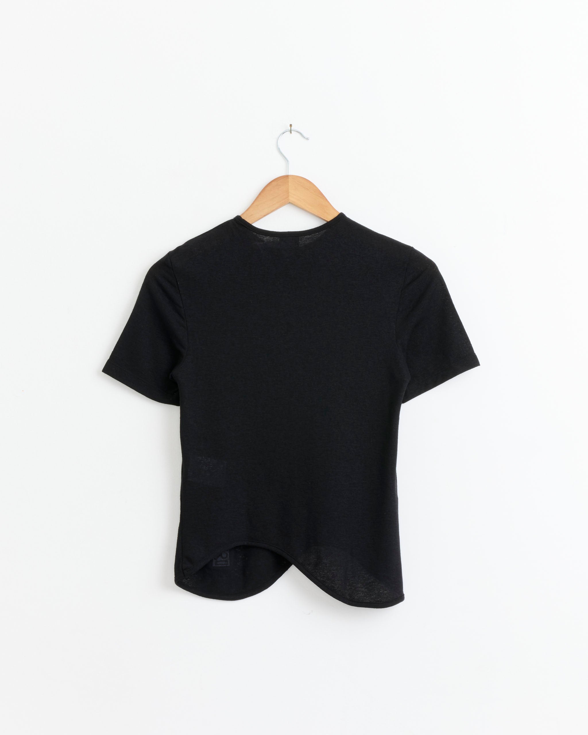 The J. Kim Ying Yang T-Shirt in Black, made from soft linen jersey with a semi-fitted cut, hangs on a wooden hanger against a white wall, shown from the back.
