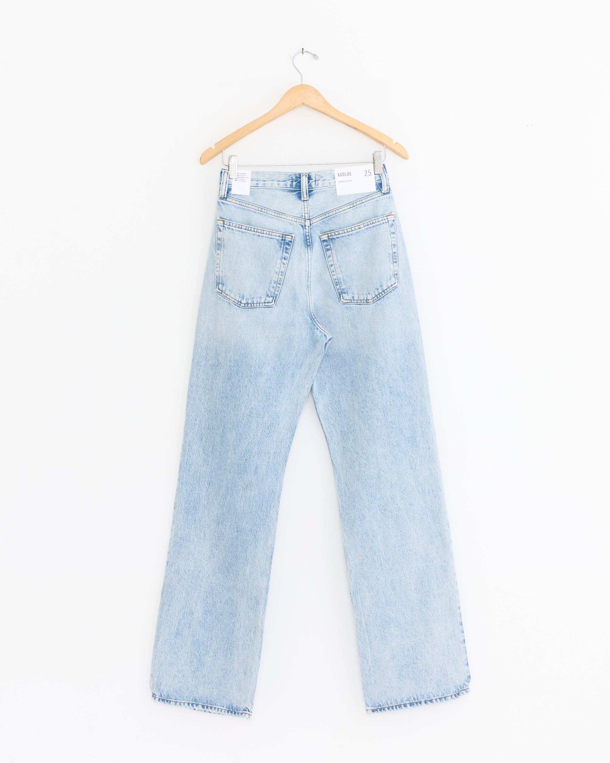 The AGOLDE Vintage Loose Jean in Detach is a light blue, high-waisted straight-leg style shown from the back on a wooden hanger, with two back pockets and a white waistband label against a plain white background.