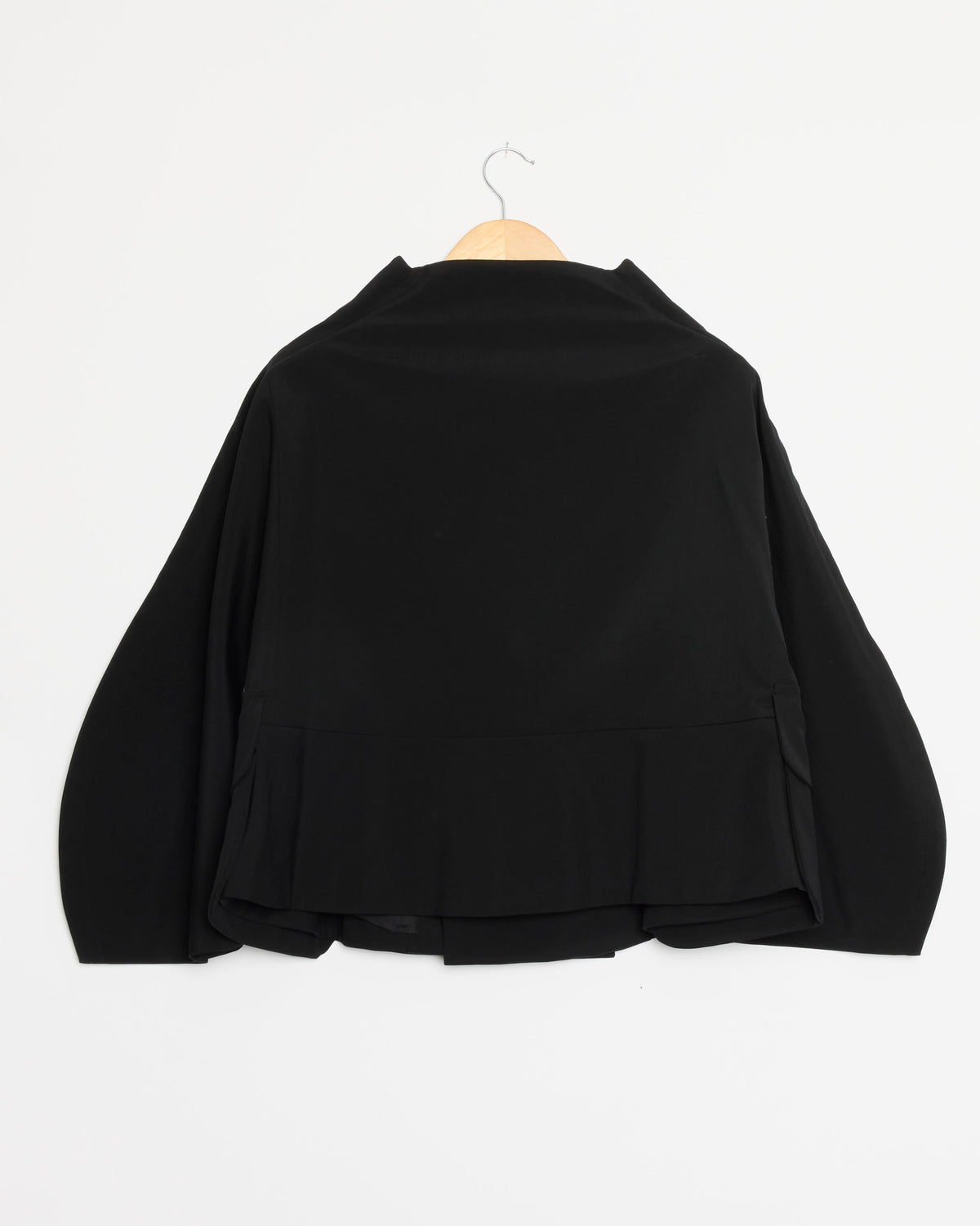 Displayed on a wooden hanger against a plain white background, the J024 Jacket in Black by Comme des Garçons Comme des Garçons features long, wide sleeves and a layered back detail.