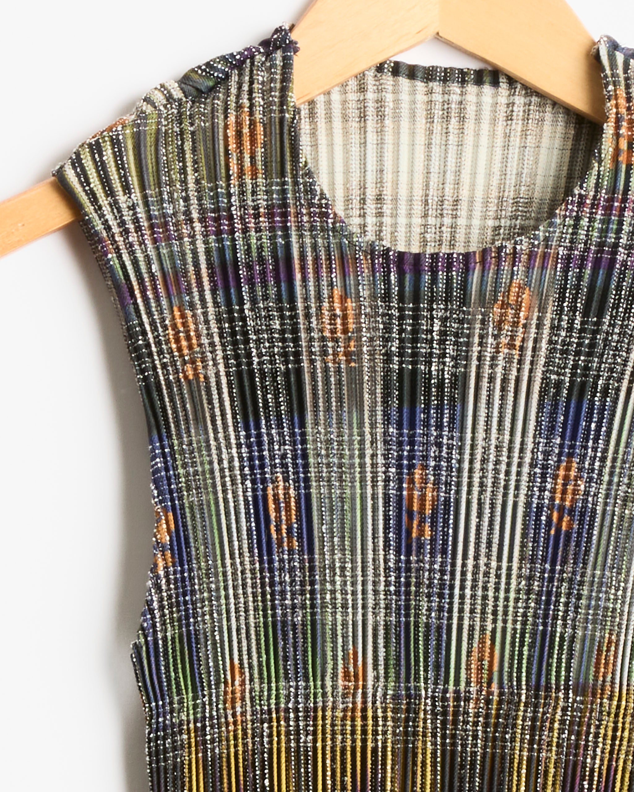 Close-up of the Julia Heuer Thelma Top in Heige, a sleeveless design with a round neckline, showcasing a multicolored plaid-inspired pattern with small orange floral accents, displayed on a wooden hanger against a white background.