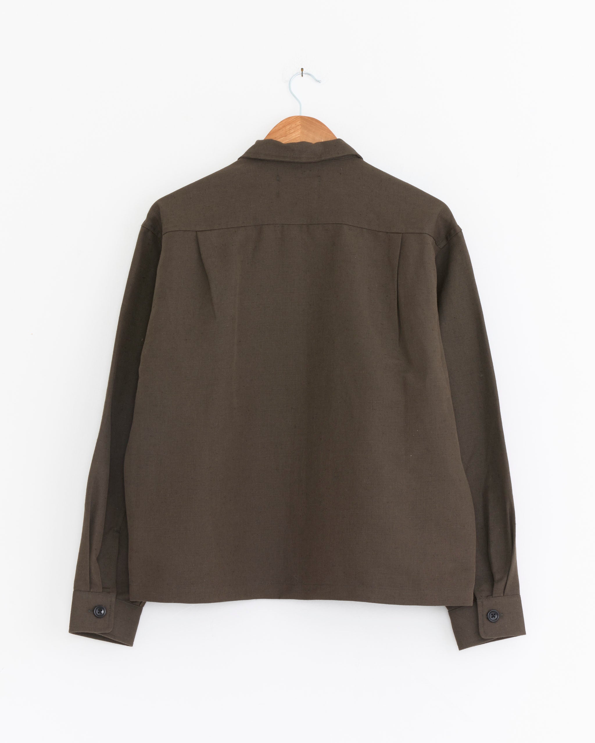 The James Coward Travail Shirt in Coffee Grounds is shown from the back, hanging on a wooden hanger against a plain white background.