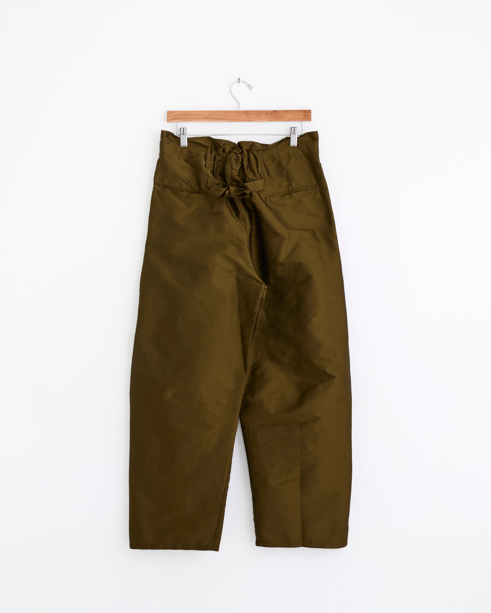 The Chan Luu Techno Taffeta Barrel Pant in Olive features a high-waisted, wide-leg silhouette with a tied waist belt, displayed on a wooden hanger against a plain white background.