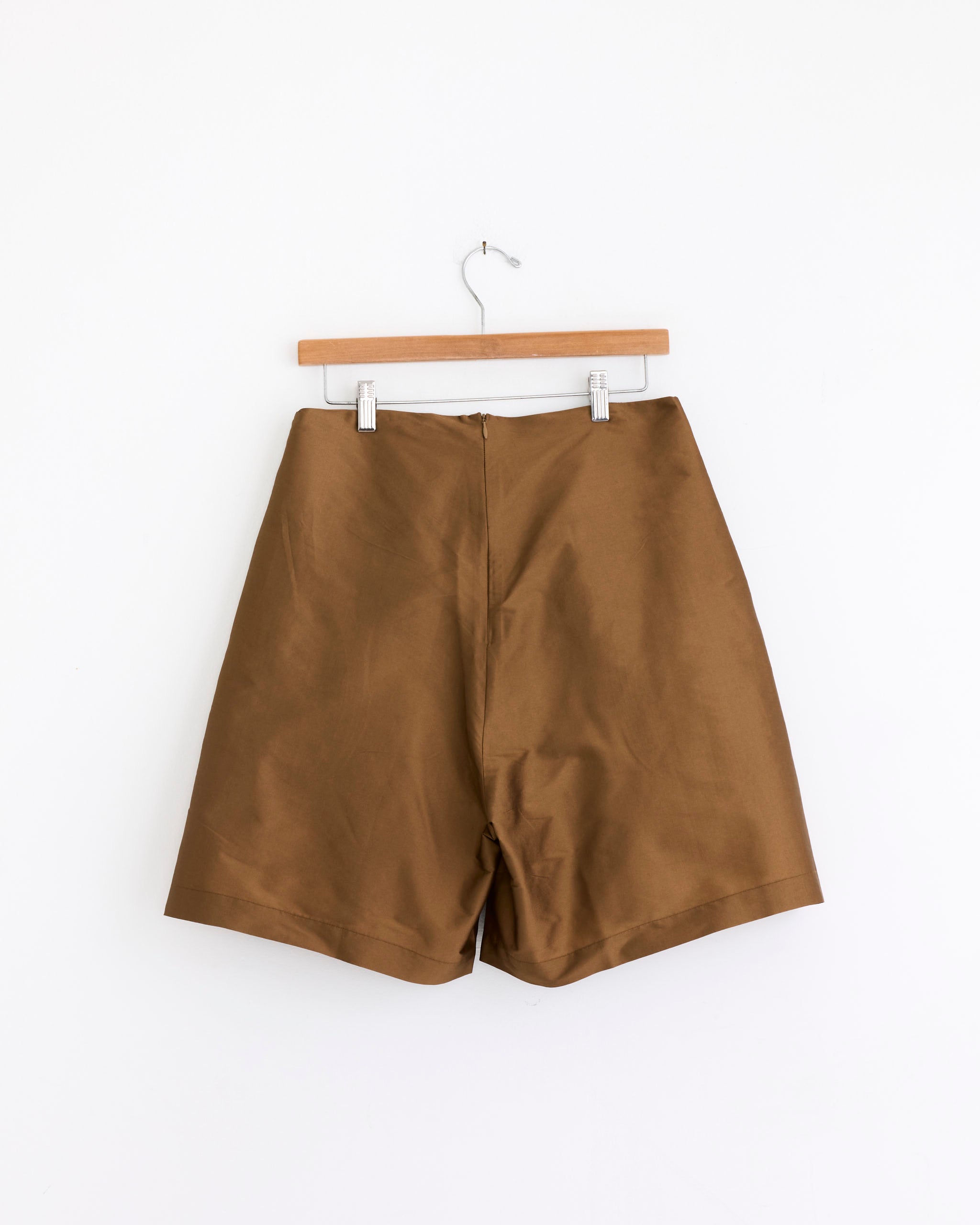 The Chan Luu Techno Taffeta Long Shorts in Bronze, featuring a high-waisted wide leg silhouette, hang on a wooden hanger against a plain white background.