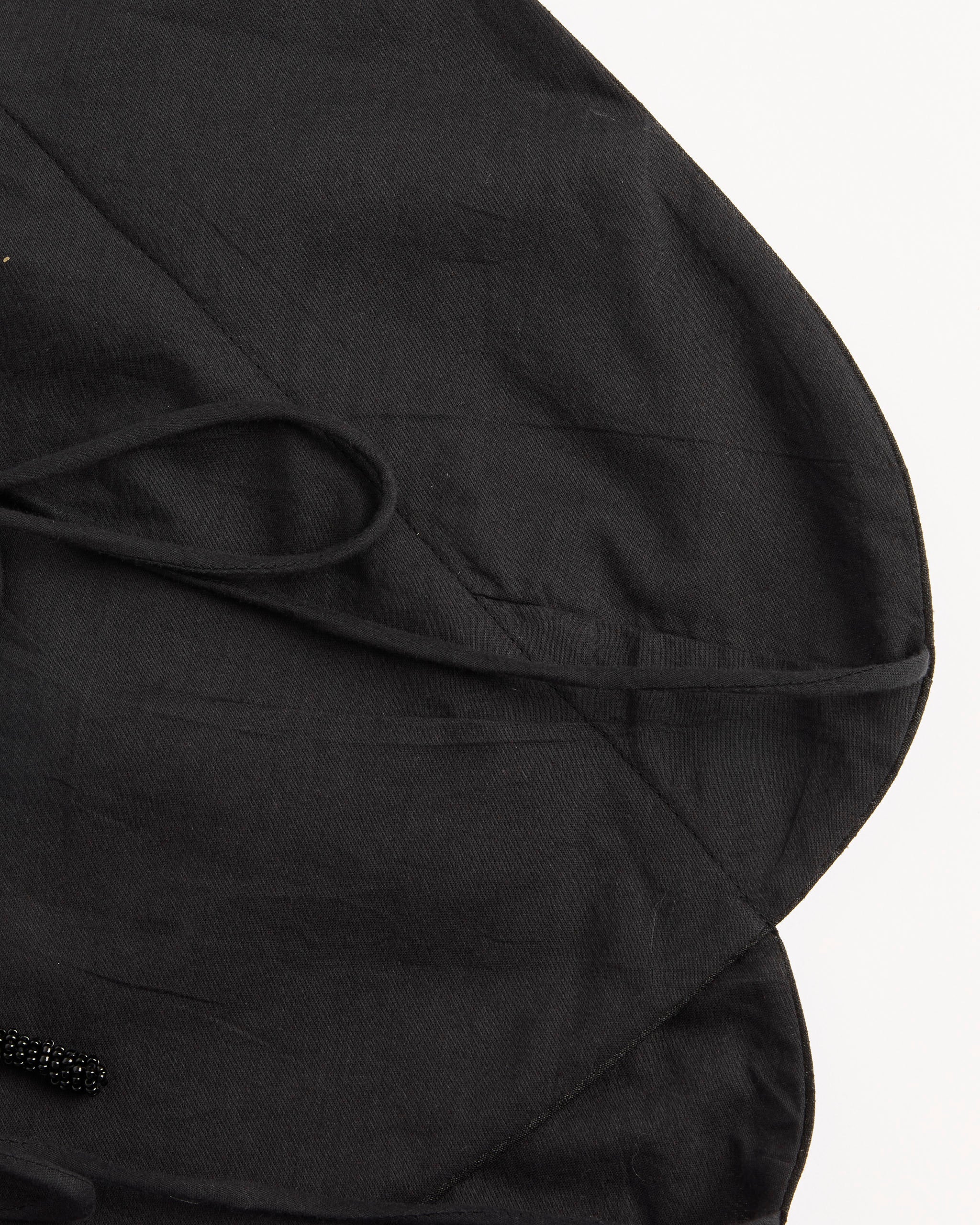 A close-up of the Chan Luu Napkin Dupioni Halter Top in Black, laid flat on a white surface, highlights its tie strap, rounded edge, seams, and visible stitching details.