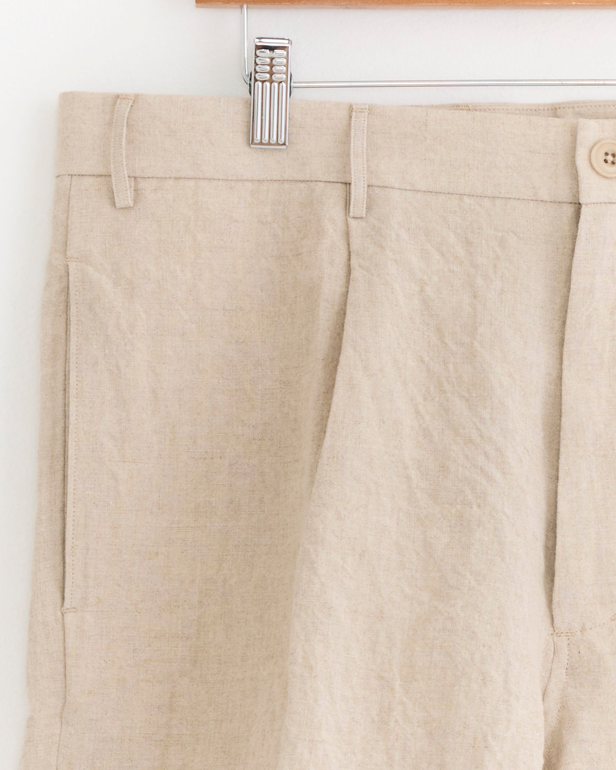 Close-up of SMOCK Arroyo Short in Sun Dried Linen Ivory, shown on a hanger with visible belt loops, pleats, side pocket, and button closure at the waistband.