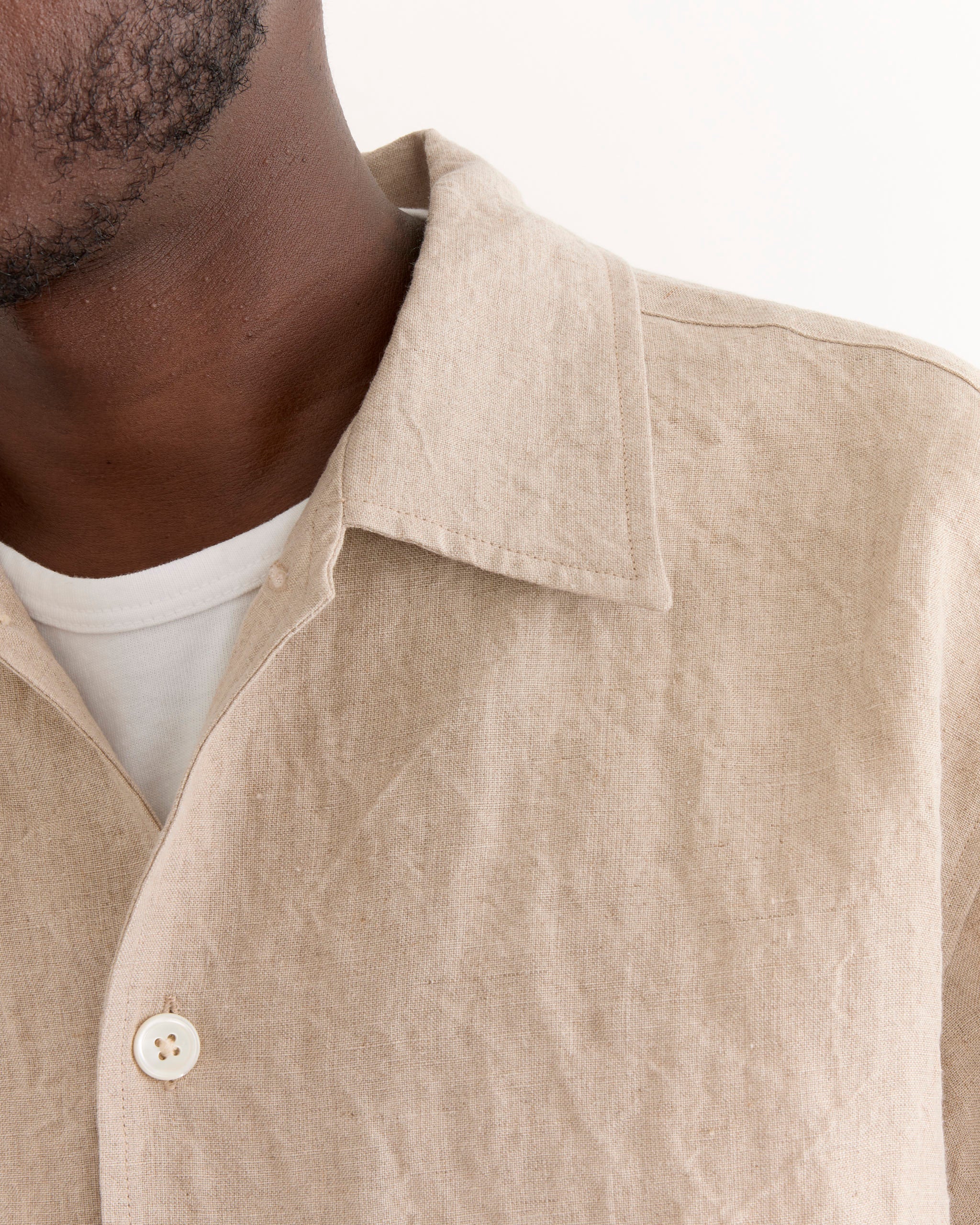 A close-up of a person wearing the SMOCK Cardiff Shirt in Sun Dried Linen Ivory over a white t-shirt, highlighting the collar, button, and texture; only part of the lower face and neck is visible.
