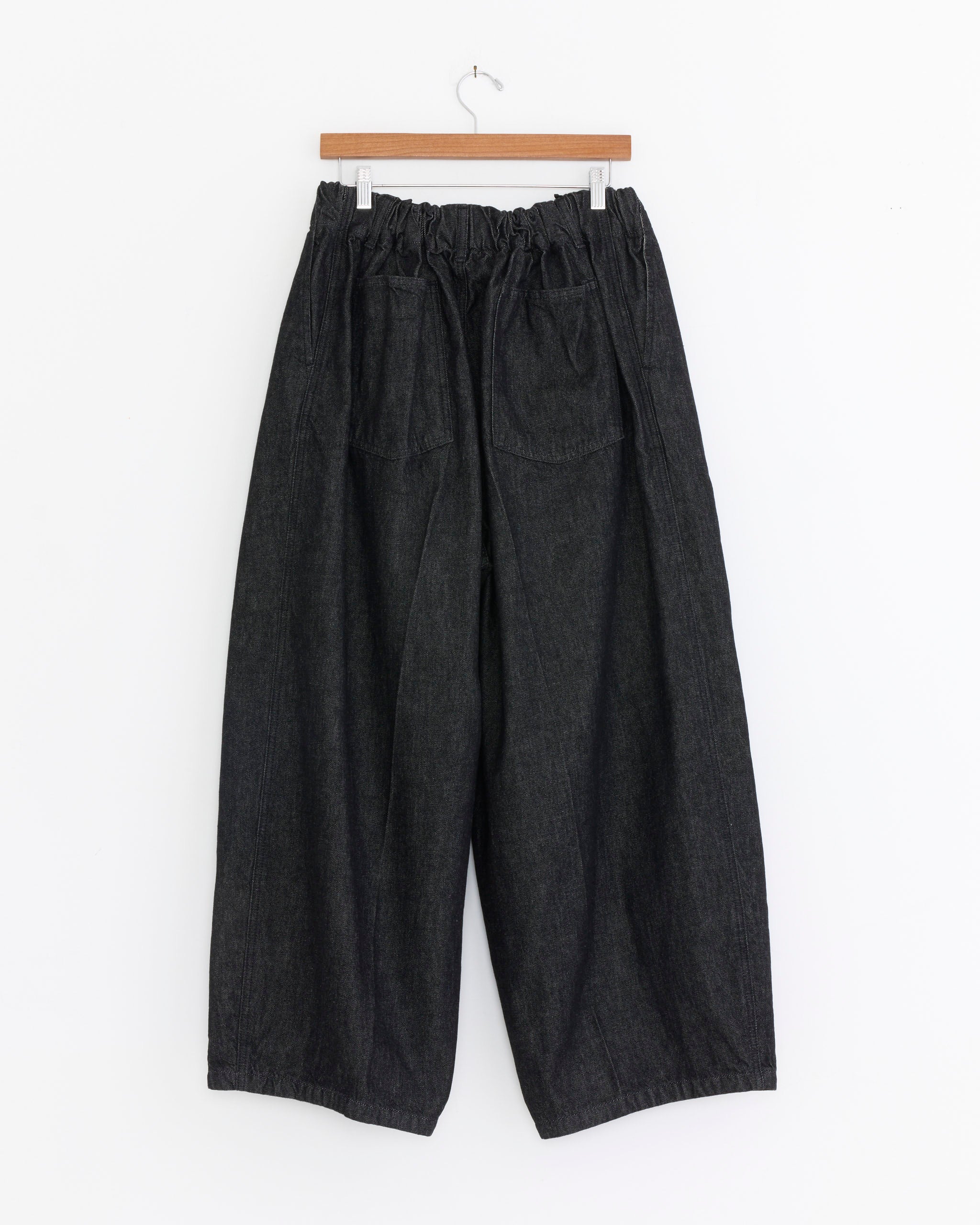 The Sillage Circular Denim Pant in Black One Wash features a wide-leg, high-waisted cut, elastic waistband, and two front pockets. Shown on a wooden hanger against a white background. Made in Japan.