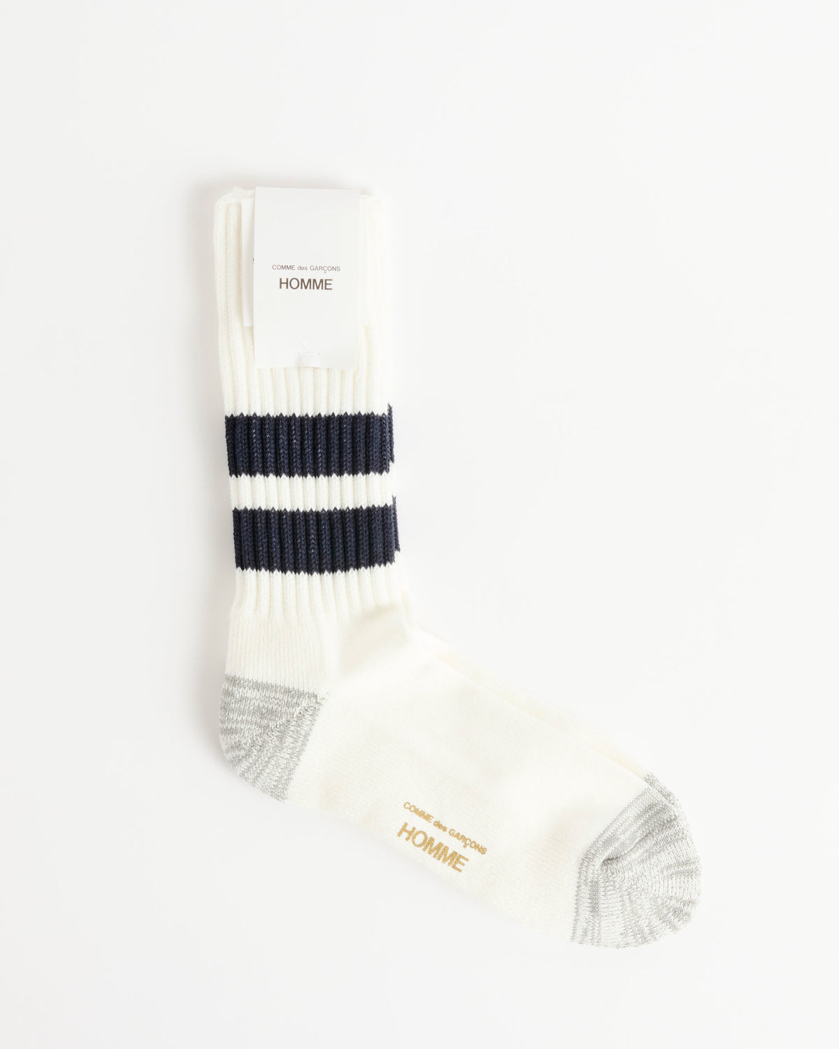 A single Comme Des Garçons Homme Socks in White/Navy, featuring two navy blue stripes, gray heel and toe, and gold HOMME text near the toe—expertly crafted as low gauge pile socks in Japan—is displayed on a plain white background.