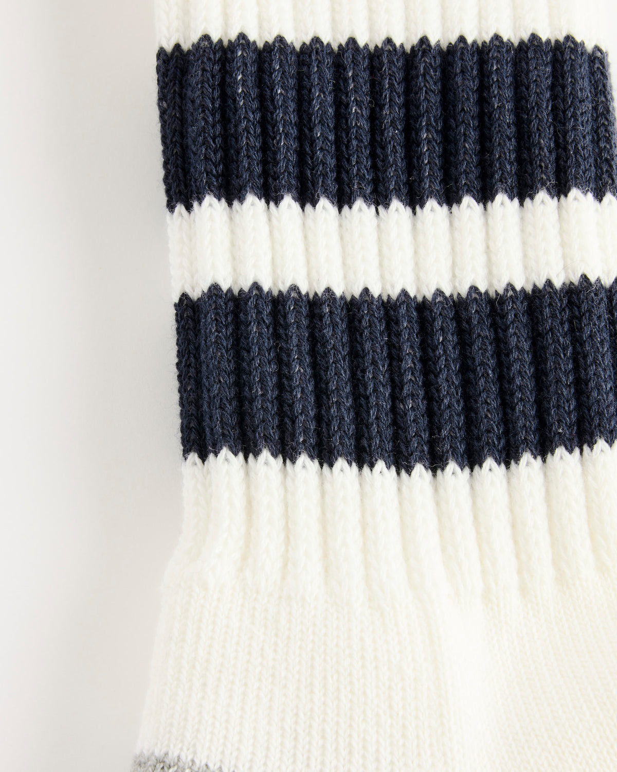 A close-up of the “Socks in White/Navy” by Comme Des Garçons Homme reveals a knitted fabric with alternating horizontal stripes of navy blue and white. The clearly visible knit pattern and texture highlight the meticulous craftsmanship characteristic of Made in Japan designs.