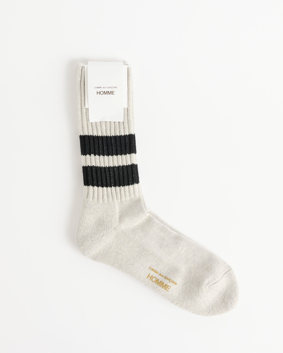 A single heather grey low gauge pile sock with two black horizontal stripes near the top, a white label reading Comme Des Garçons Homme, and gold text printed on the foot—made in Japan—lying on a white background.