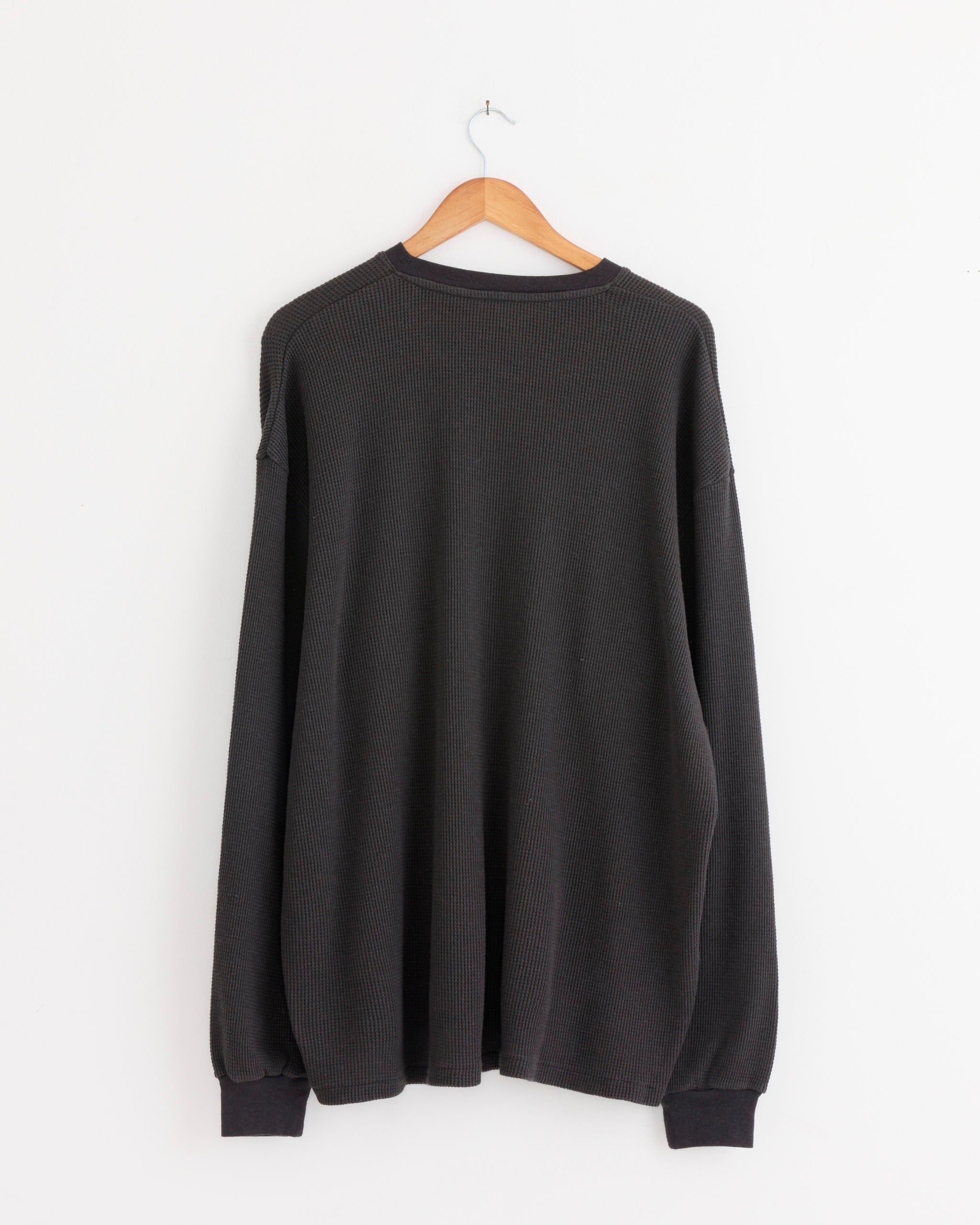 The A.PRESSE Cashmere Blend Waffle L/S Henley Shirt in Charcoal, featuring ribbed cuffs, is displayed from the back on a wooden hanger against a plain white wall.