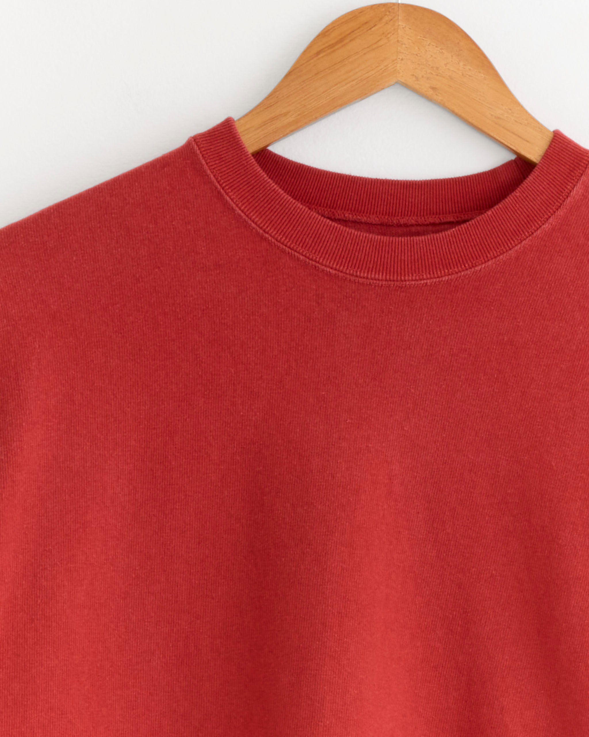 A close-up of the A.PRESSE Vintage Long Sleeve T-Shirt in Red on a wooden hanger, hanging against a white wall.