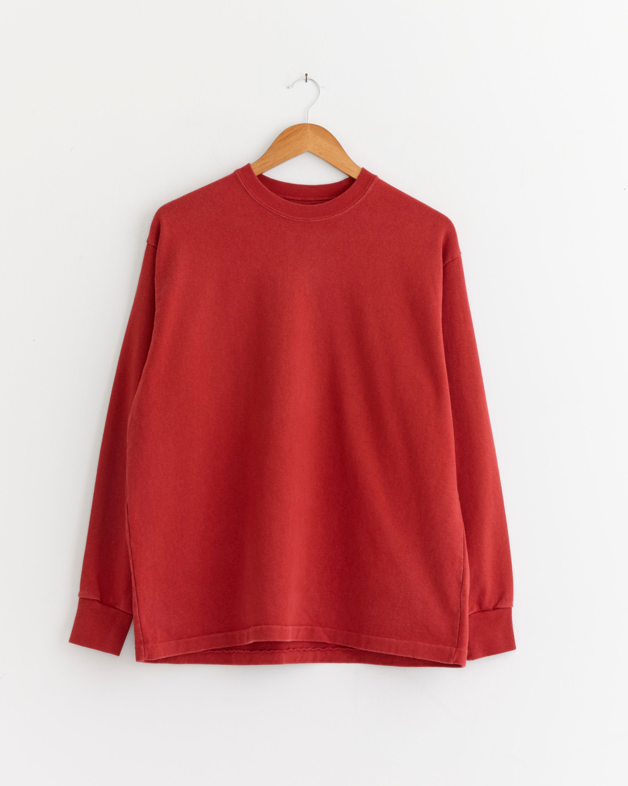 The A.PRESSE Vintage Long Sleeve T-Shirt in Red hangs on a wooden hanger against a white wall.
