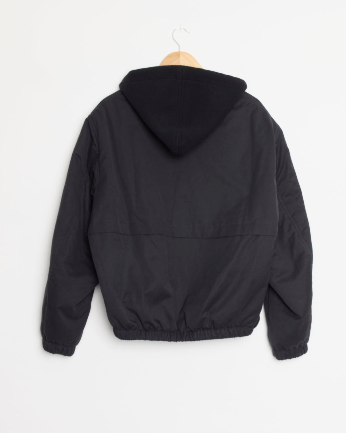 A navy Hooded Bomber Jacket by Salon C. Lundman hangs on a wooden hanger against a plain white background, shown from the back with elastic cuffs and waistband.