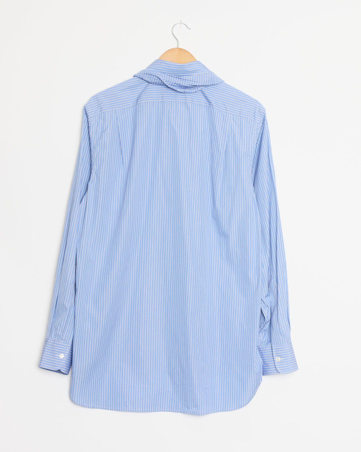 The Bandana Shirt in Fine Polo Stripe by Salon C. Lundman—a light blue and white, long-sleeve cotton shirt featuring fine polo stripes—is shown hanging on a wooden hanger with the back facing forward against a plain white background.