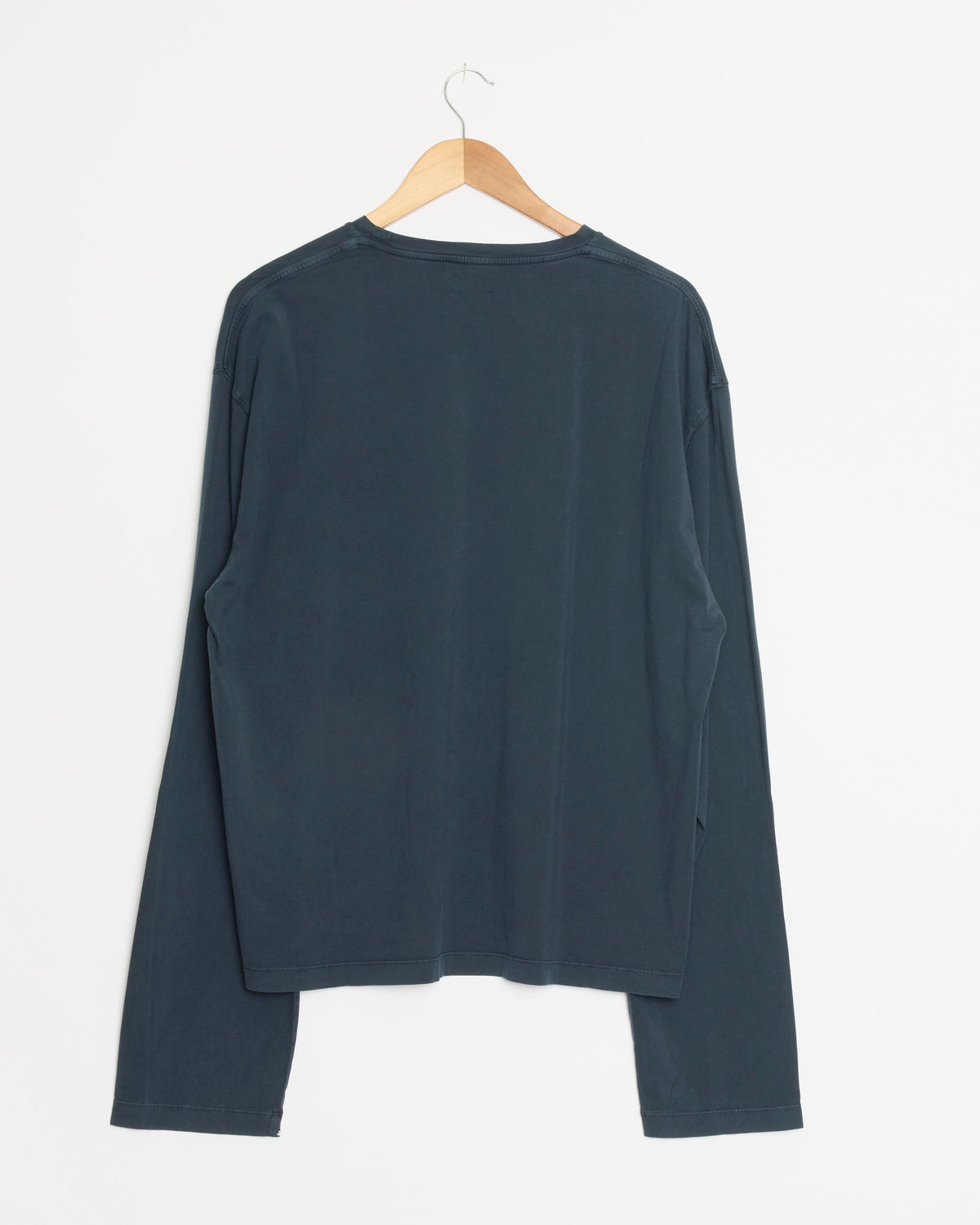A Salon C. Lundman Organic Cotton T-Shirt in Faded Blue, crafted in Italy, hangs on a wooden hanger against a plain white wall, displayed from the back.