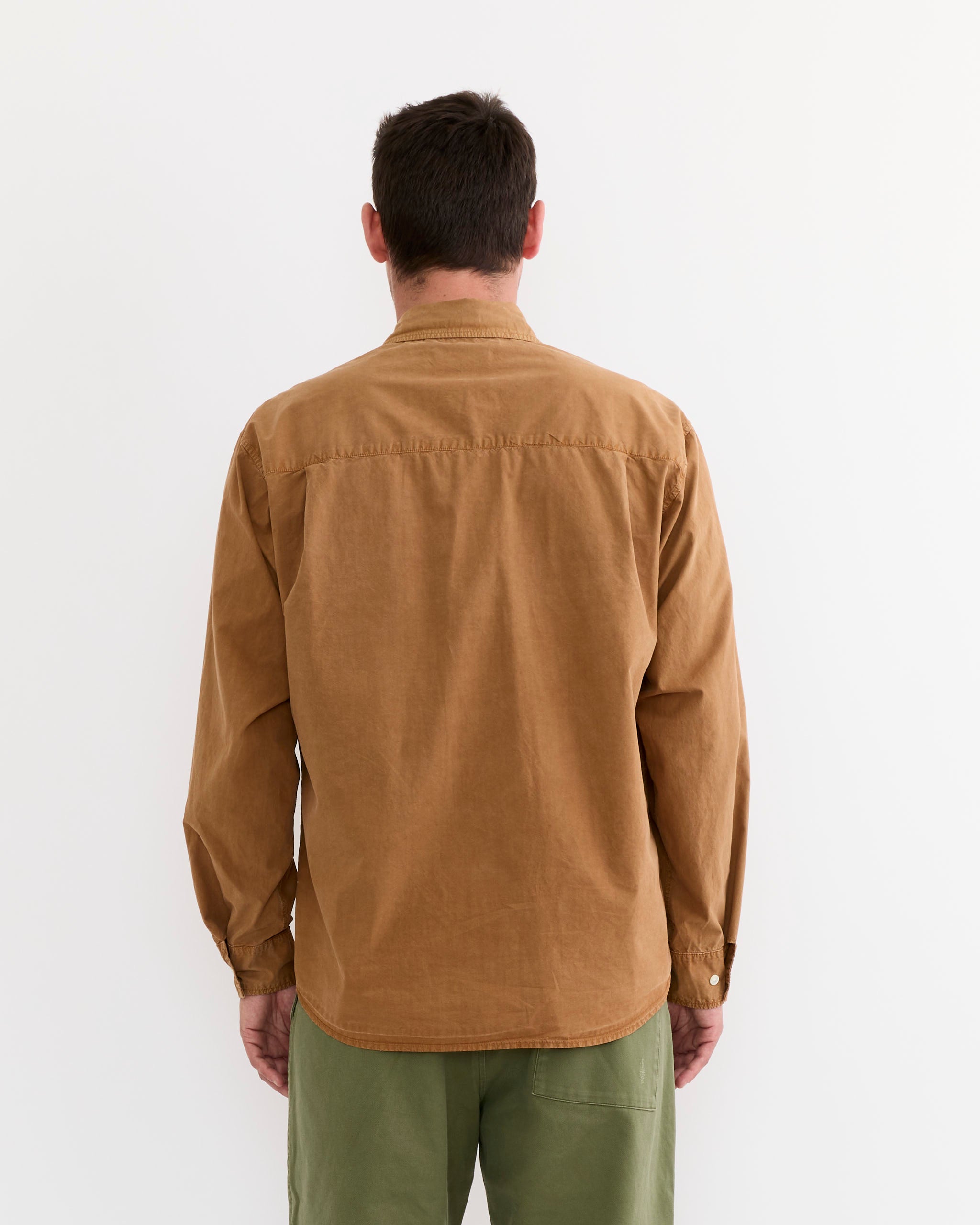 A person faces away from the camera wearing the SMOCK Routine Shirt in Cotton Silk Washed Chestnut and olive green pants, both set against a plain white background.