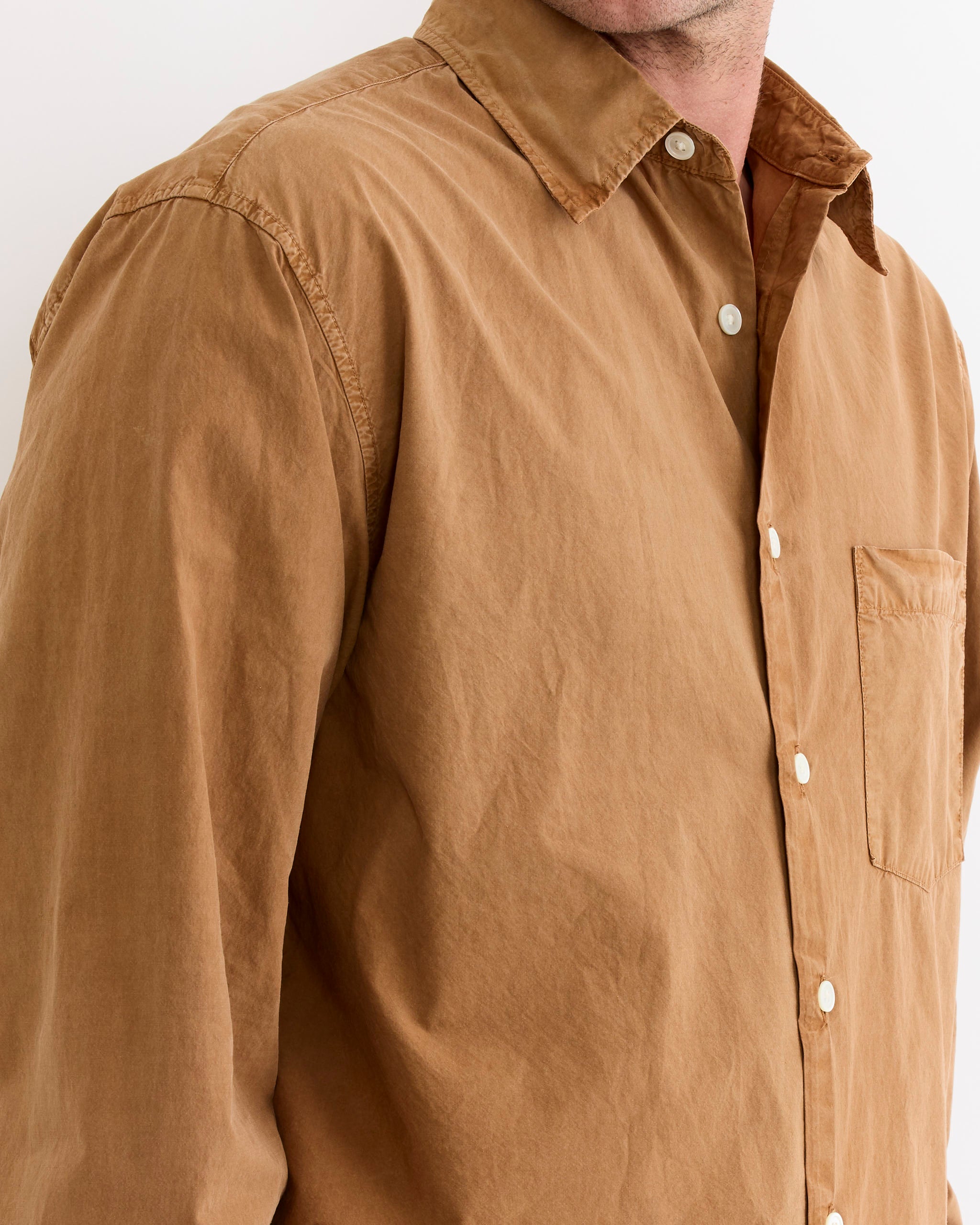 A man wears the SMOCK Routine Shirt in Cotton Silk Washed Chestnut, a garment-dyed light brown button-up with a chest pocket, shown from shoulders to mid-torso against a plain background.
