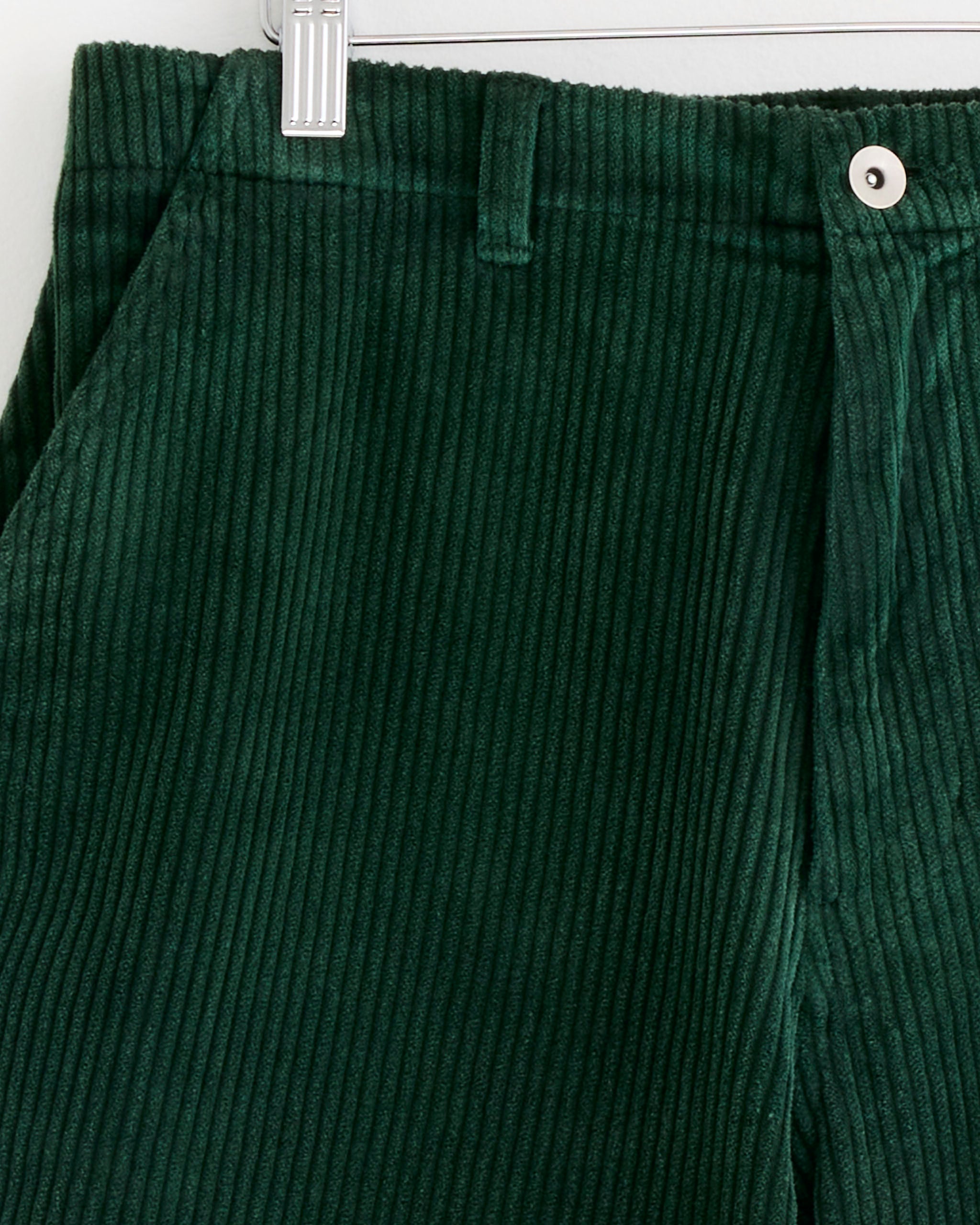 Close-up of the SMOCK Laguna Short in Corduroy Washed Green, highlighting its ribbed cotton texture, waistband with a belt loop, and white button closure on a hanger.