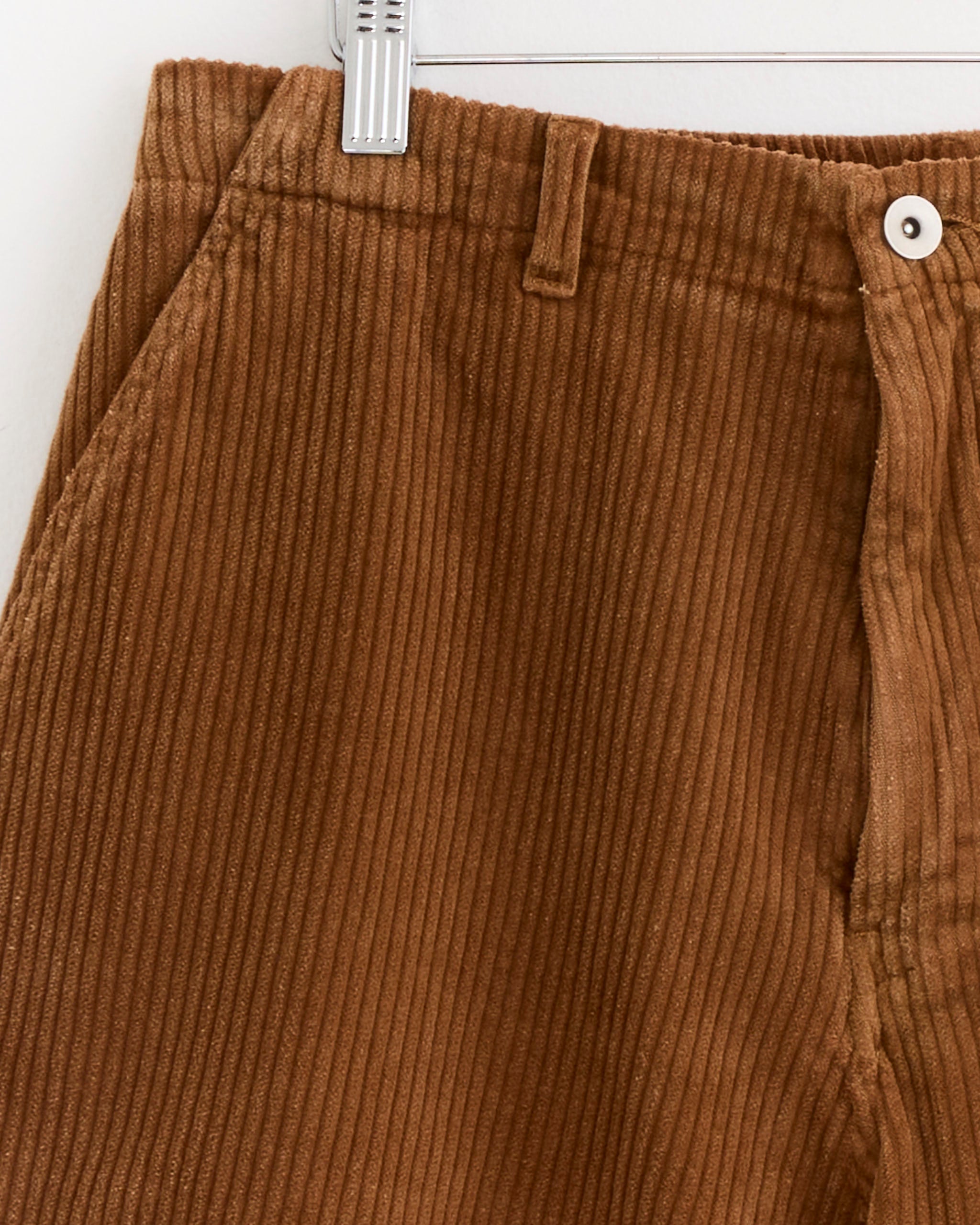 Close-up of SMOCK's Laguna Short in Corduroy Washed Chestnut, made in Los Angeles, hanging on a hanger and highlighting the waistband, side pocket, button closure, and vertical ribbed texture.