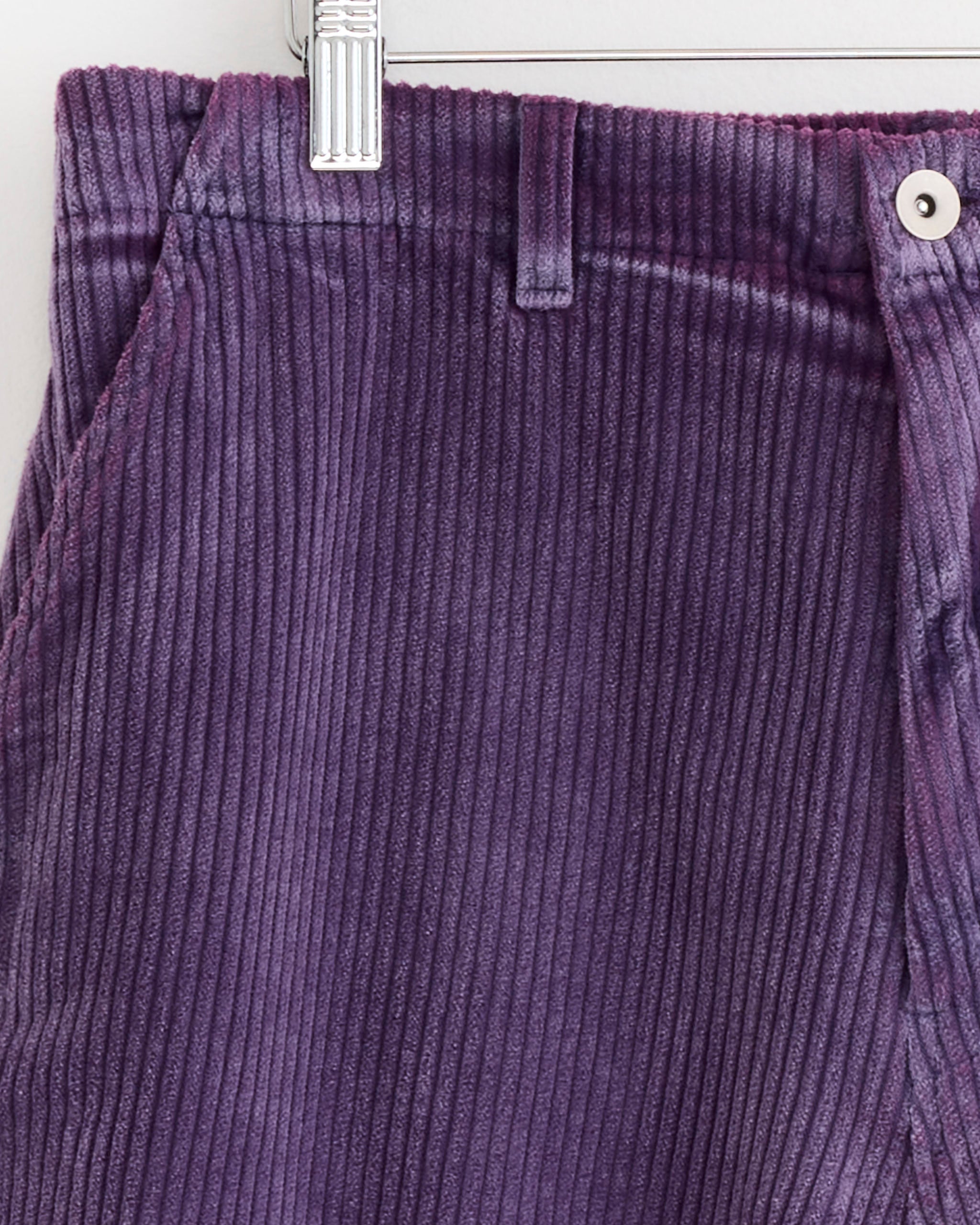 Close-up of SMOCK’s Laguna Short in Corduroy Washed Purple, featuring vertical ribbed texture, front pocket, belt-loop waistband, and button—expertly crafted in Los Angeles and hung on a metal hanger.
