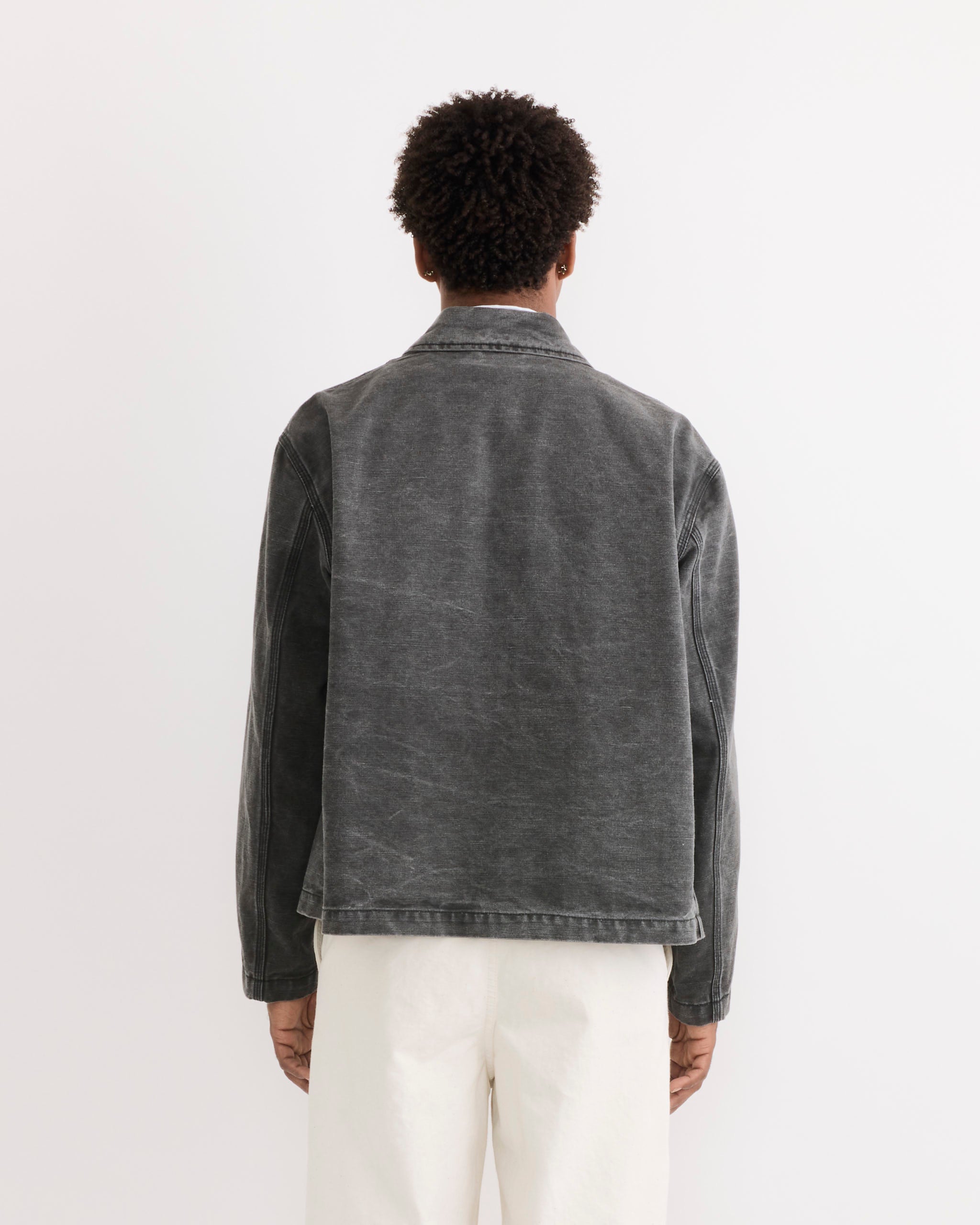 A person with short curly hair faces away from the camera, wearing the SMOCK Triple Stitch Hydra Jacket in washed pigment dyed cotton grey—ideal inspiration for anyone looking for fit ideas or sizing tips.
