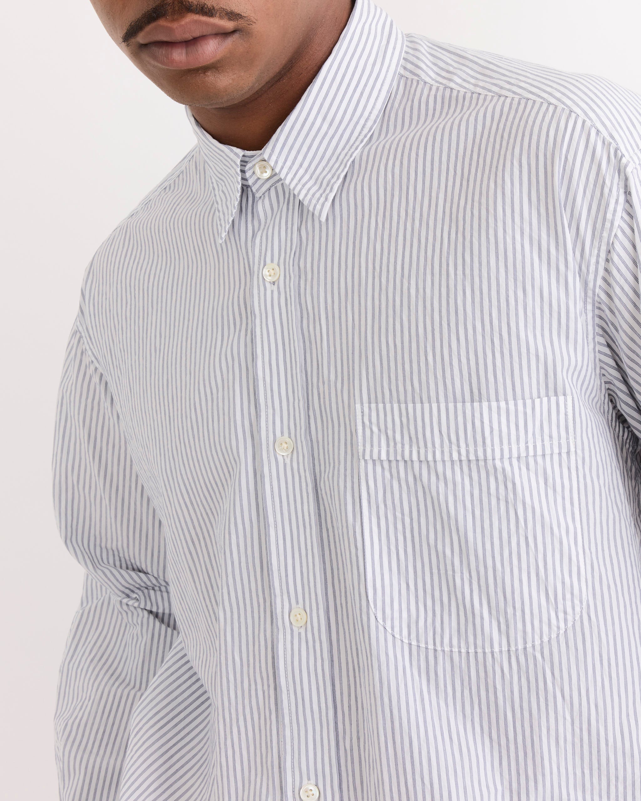 A person wearing the SMOCK Gio Shirt in Crushed Cotton in Navy Stripe Ni, featuring navy and white vertical stripes and a single chest pocket; shown from shoulders to mid-torso with face partially visible.