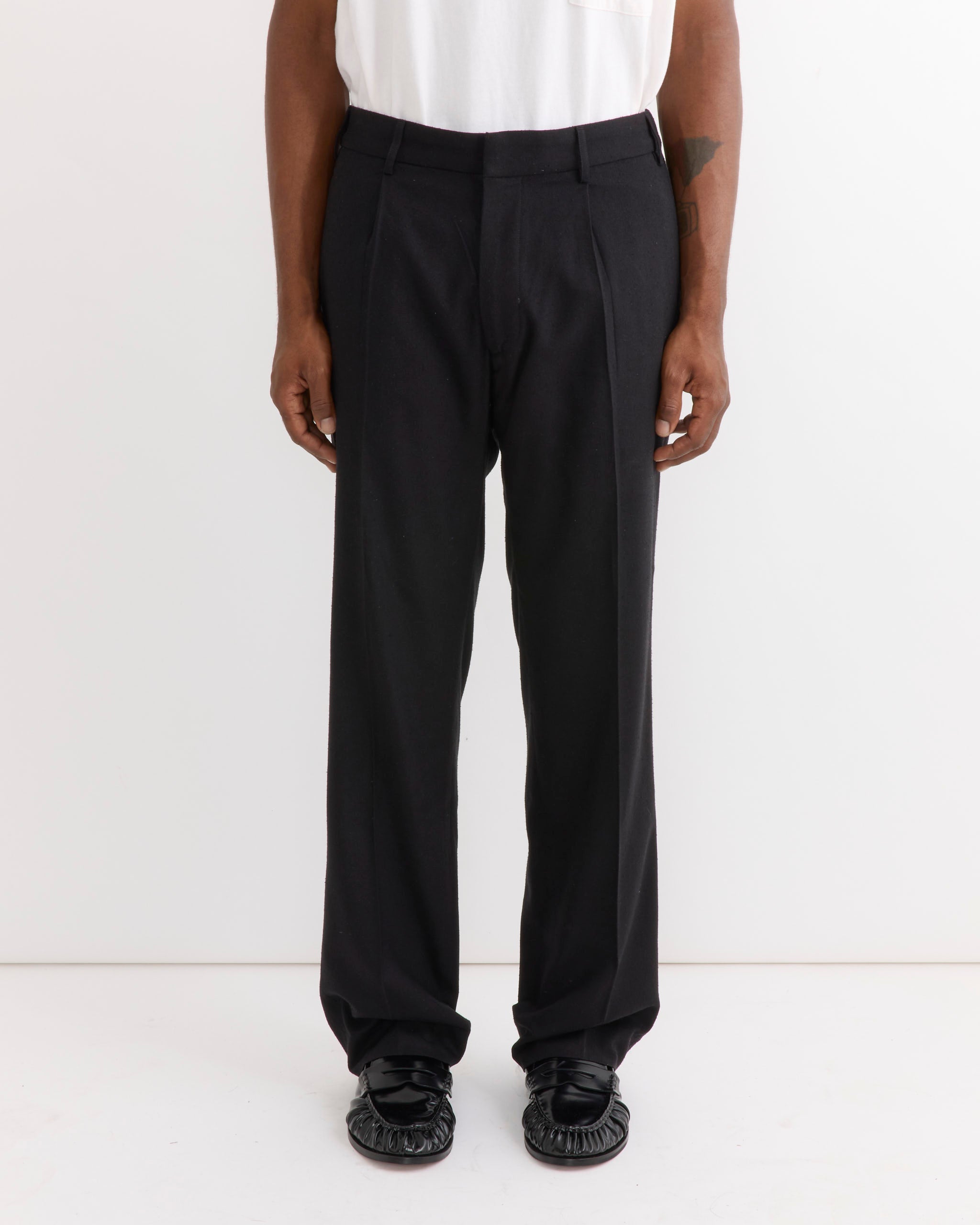A person stands against a white background, wearing a white shirt tucked into the SMOCK West Coast Pant in Raw Silk Black, paired with black shoes. Only the body from shoulders down is visible.