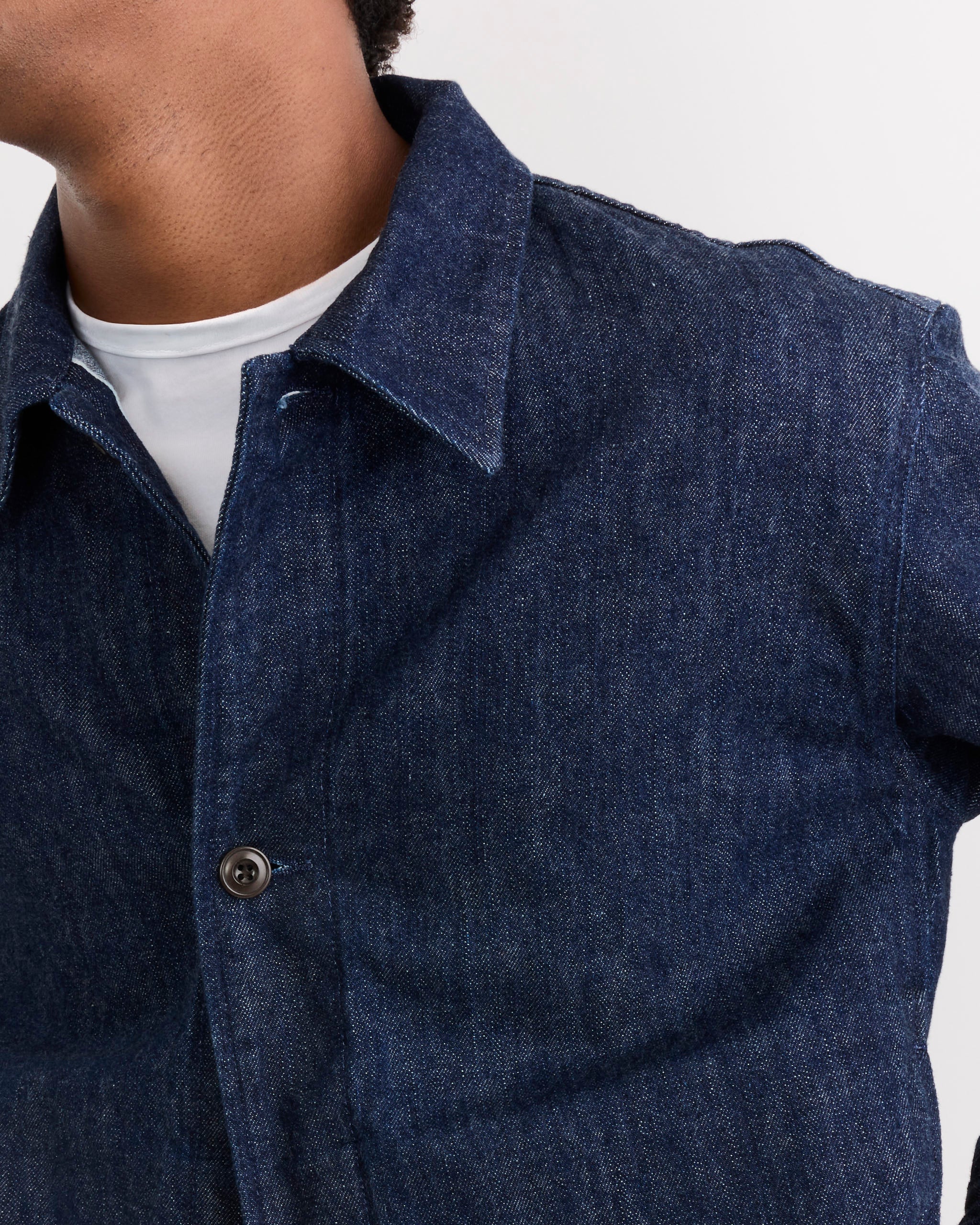Close-up of a person wearing the SMOCK Lang Jacket in Selvedge Denim Dark Blue over a white T-shirt, highlighting the fit. Only the lower half of the face, neck, and upper torso are visible against a plain background.