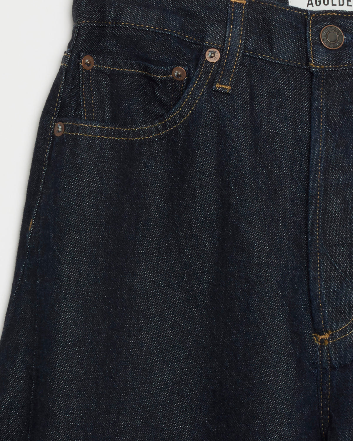 Close-up of the AGOLDE Luna Pieced Jean in Rinse, showcasing dark blue denim with visible pockets, copper rivets, gold stitching, and a partial white AGOLDE label above the waistband. Made from weightless denim, these jeans offer a flattering high-rise waist for timeless style and all-day comfort.