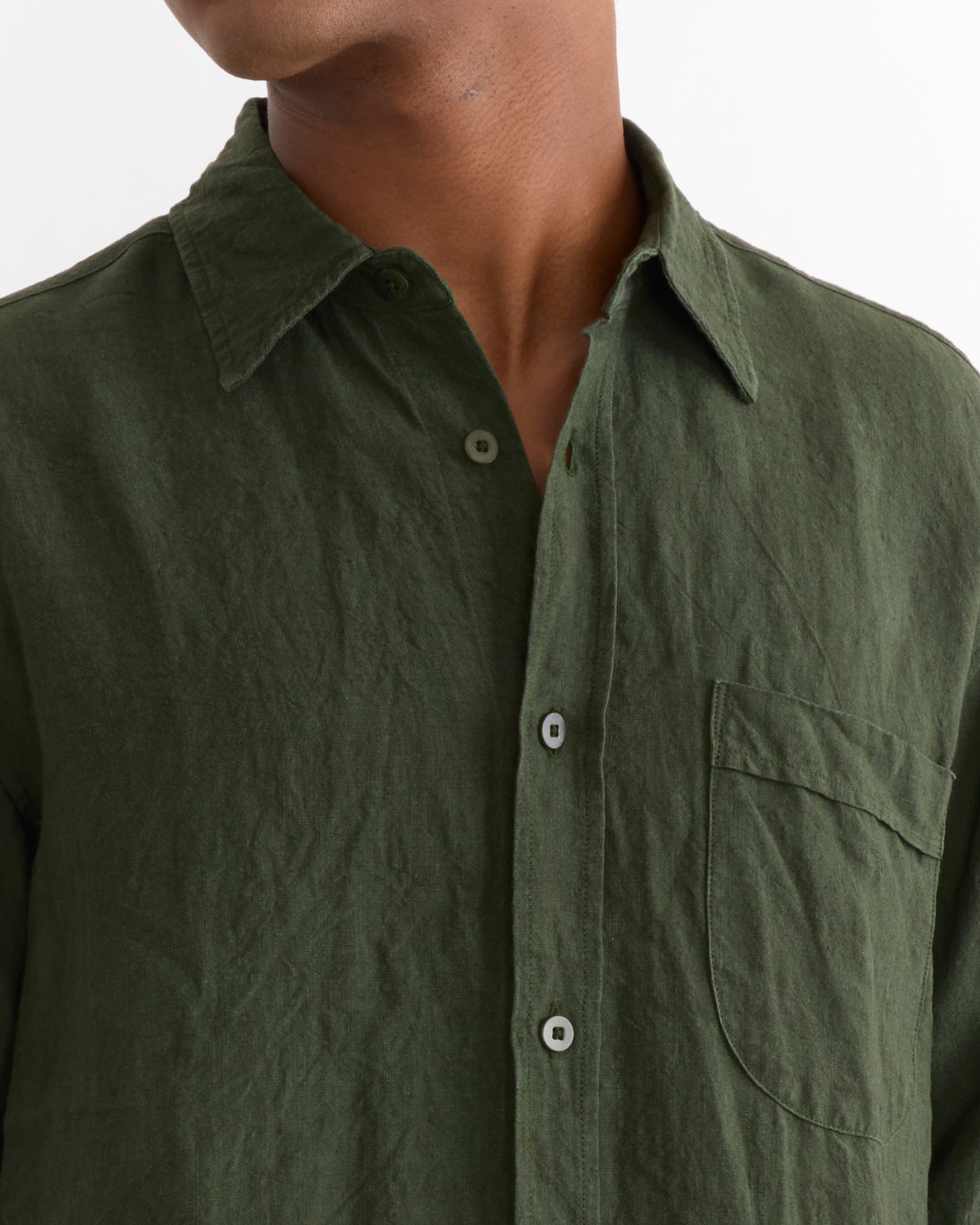 A person wearing the SMOCK Gio Shirt in Sun Dried Linen Green, featuring a chest pocket and a softly wrinkled texture, shown from the shoulders to mid-chest against a plain white background.
