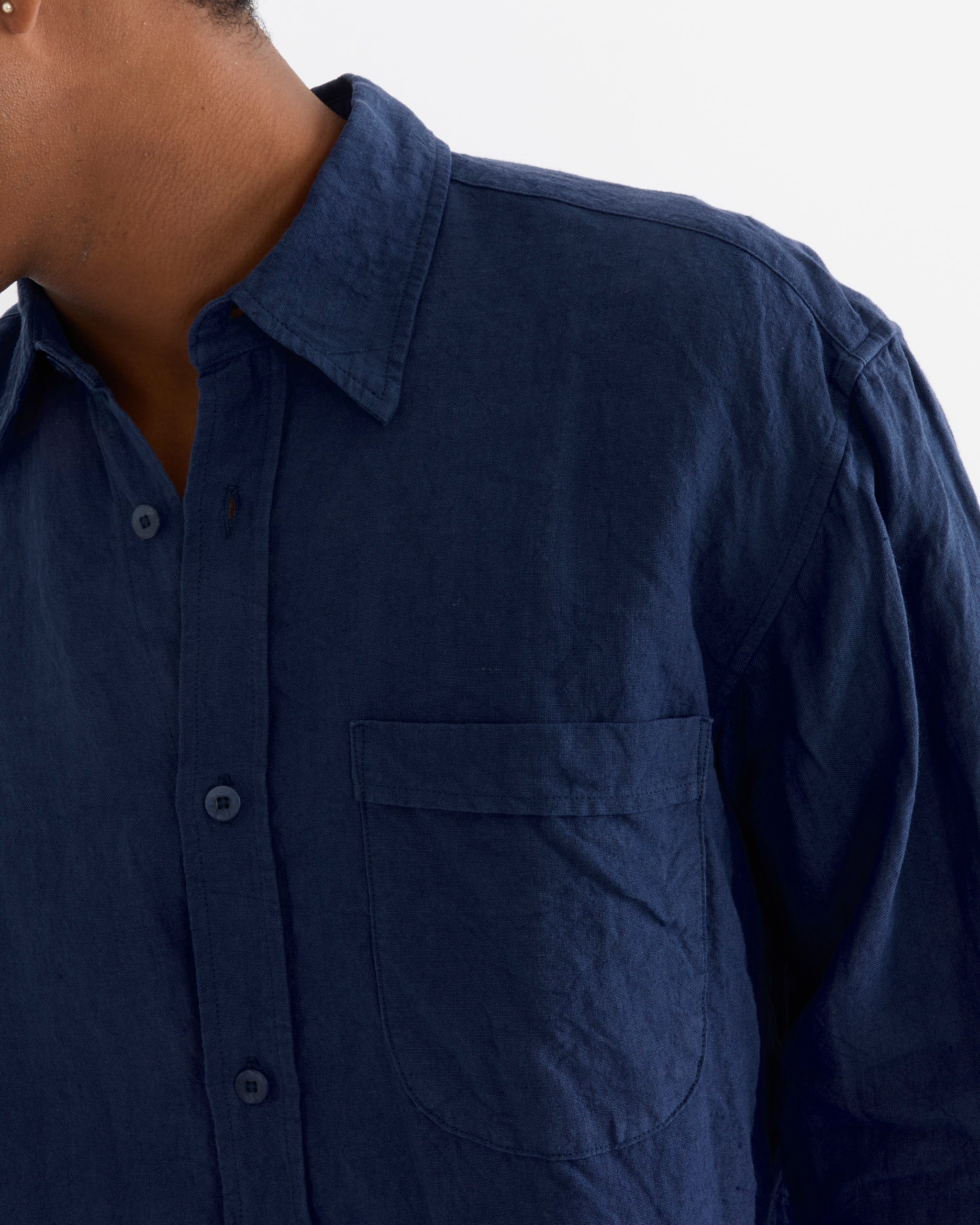 A person is shown from the shoulders to mid-torso, facing left against a plain white background, wearing the SMOCK Gio Shirt in Sun Dried Linen Blue, which features a collar and a chest pocket.