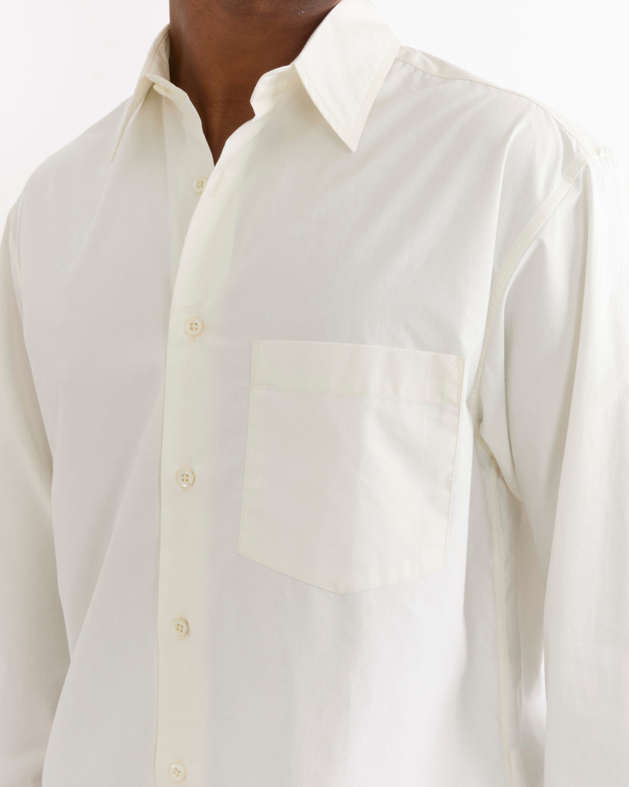 A person wearing the SMOCK Routine Shirt in Cotton Silk Off White, which features a chest pocket, stands against a plain white background. Only the torso and part of the neck and chin are visible.