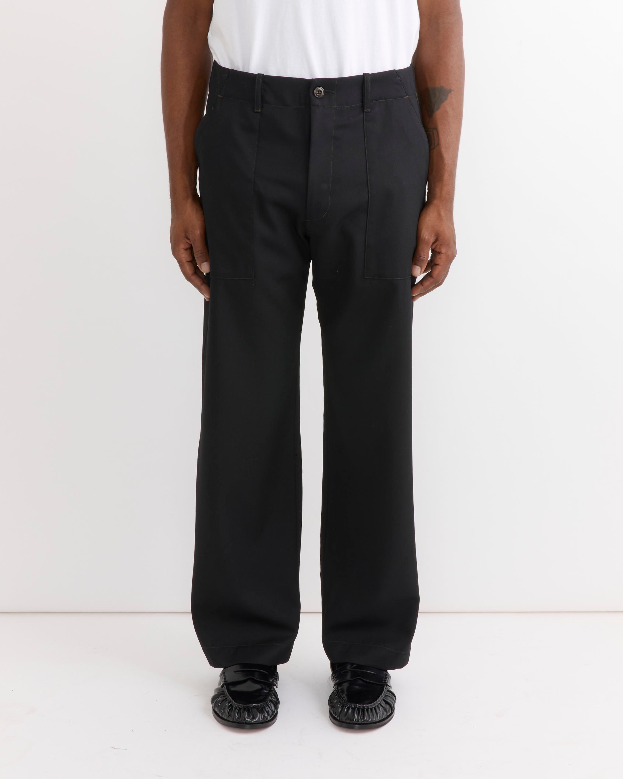 A person wearing the SMOCK Toyon Pant in Wool Gabardine Black, featuring a relaxed straight-leg silhouette, styled with a white shirt and black shoes. The image shows only the lower half of the body against a plain white background.