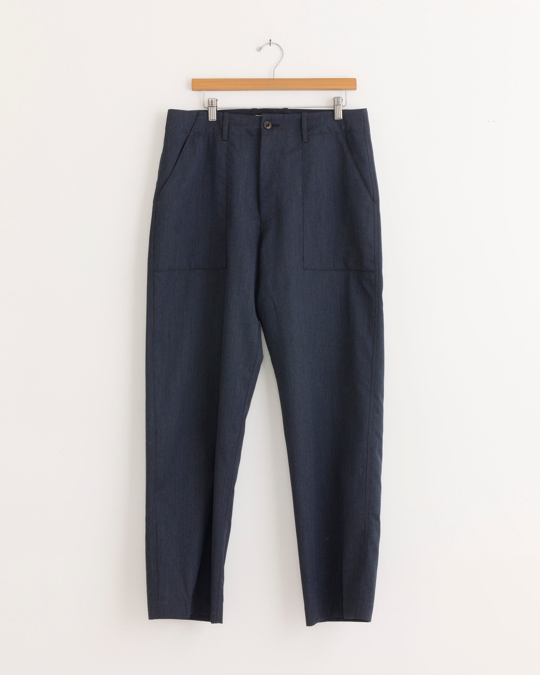 A pair of SMOCK Toyon Pants in Wool Gabardine Heather Navy, featuring a relaxed straight-leg fit and front pockets, hangs on a wooden hanger against a white background.