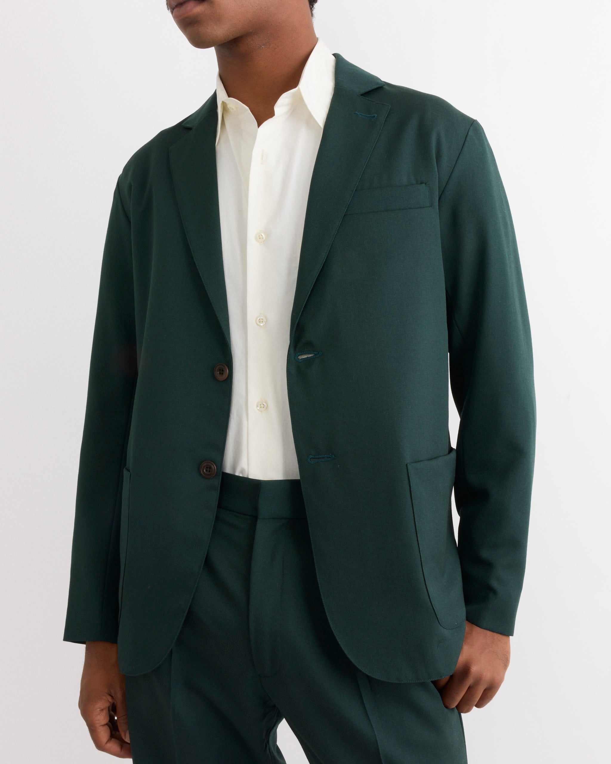A person wearing the SMOCK Blazer in Wool Gabardine Dark Green, paired with matching trousers and a white button-up shirt, stands against a plain white background.
