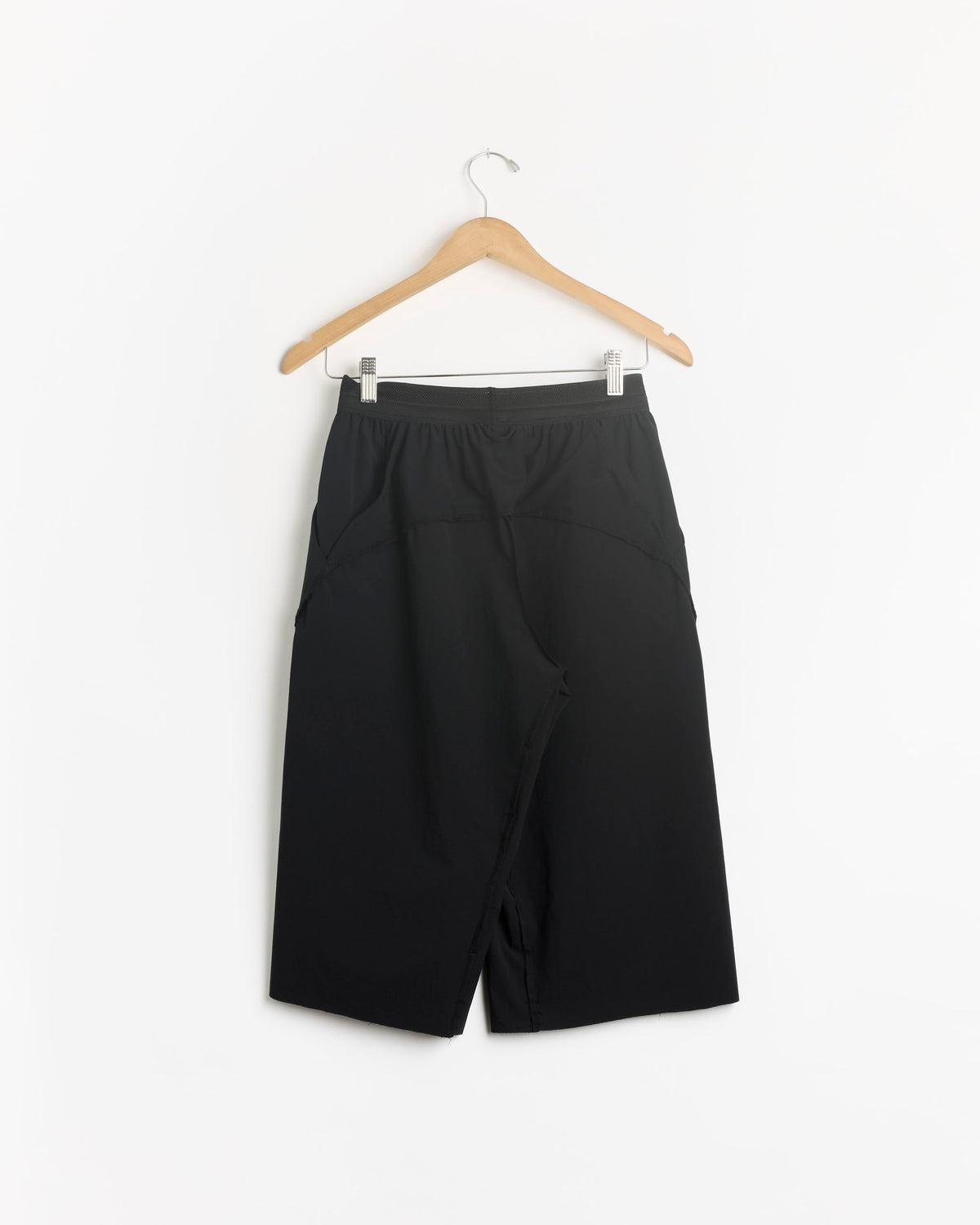 The Short in Black by Shade, featuring a knee-length athletic design, hangs on a wooden hanger against a white background.