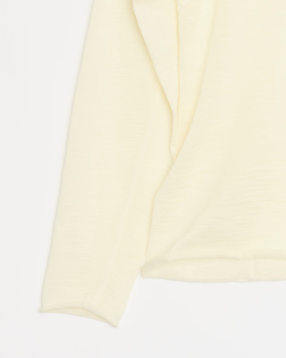 A close-up of the Shade Long Sleeve in Natural, a light yellow textured shirt crafted from Italian-milled merino wool, laid flat on a white background with part of the torso and one sleeve visible.