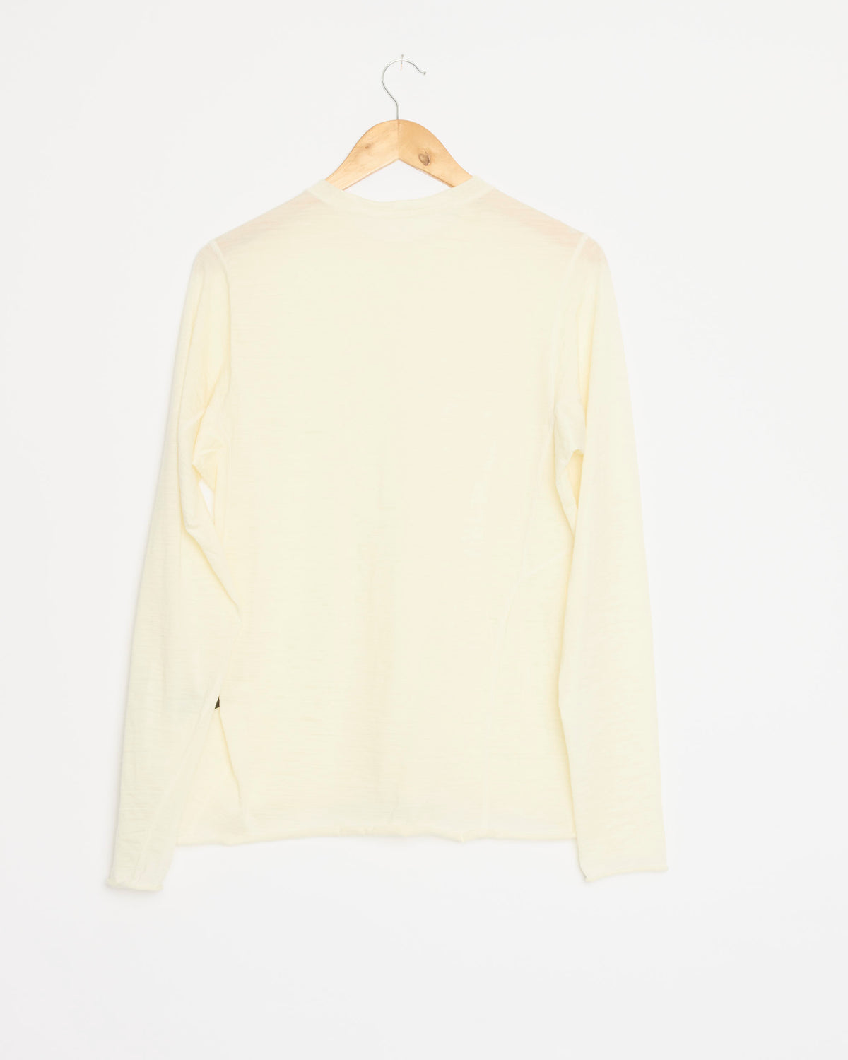 A Shade Long Sleeve in Natural, crafted from Italian-milled merino wool in a light cream shade, hangs on a wooden hanger against a plain white background, shown from the back.