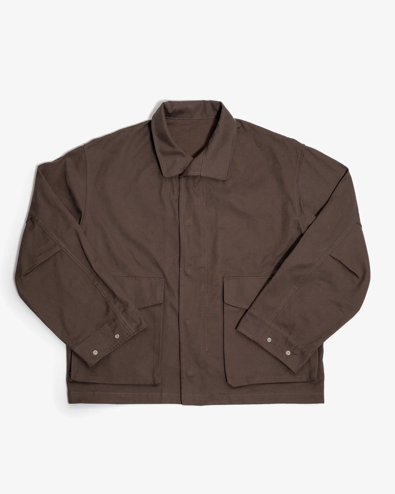 The Six Jacket in Brown by James Coward, made from durable British cotton canvas with large front pockets and buttoned cuffs, is shown laid flat on a white background.