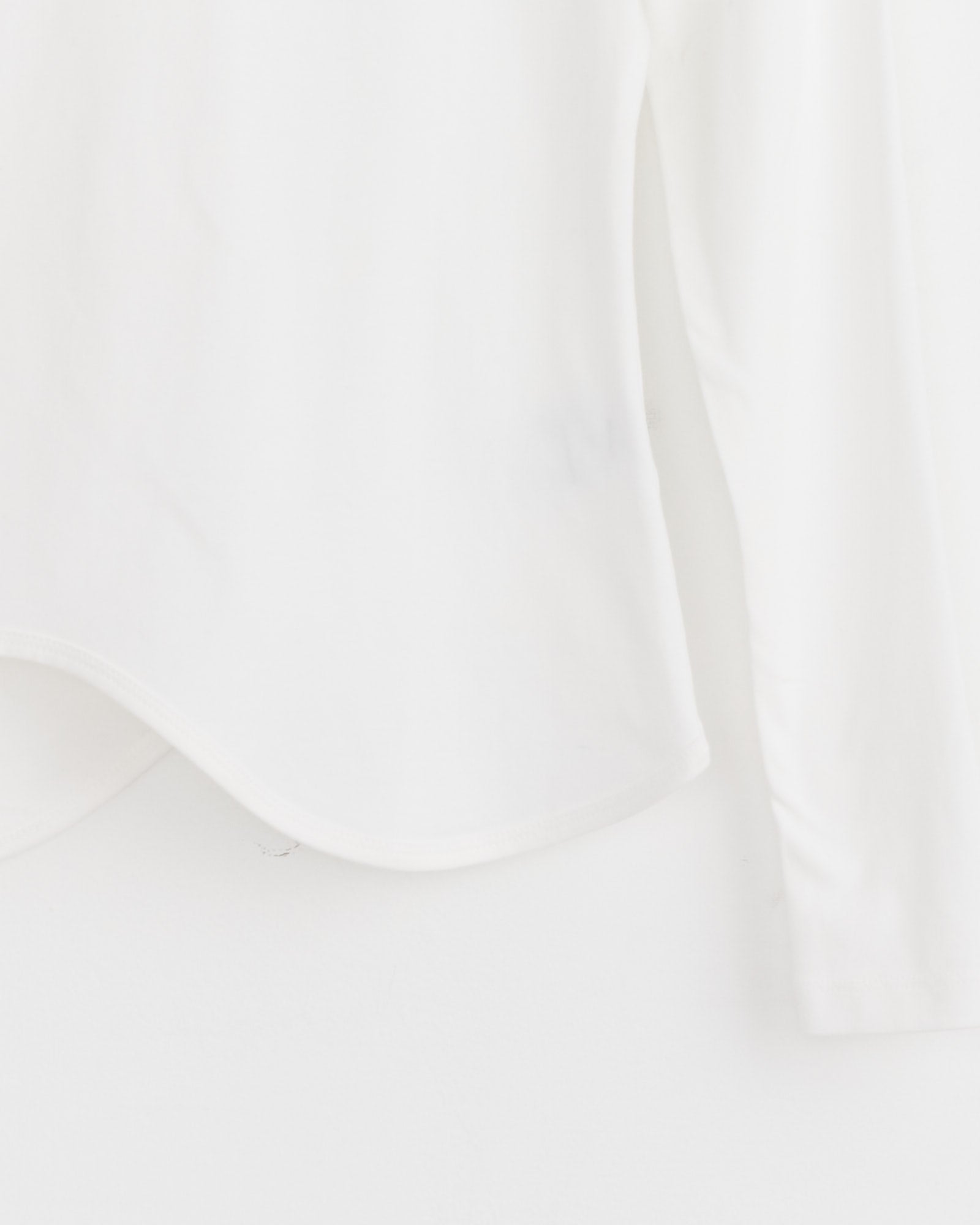 A close-up of the J. Kim Ying-Yang Top in White, crafted from a cotton blend, hangs against a white background, emphasizing its minimal hem and sleeve details.