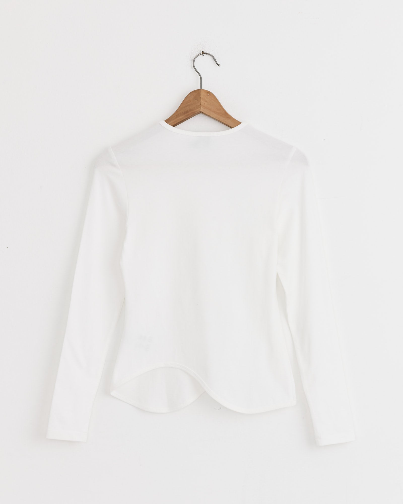 The J. Kim Ying-Yang Top in White is a long-sleeved shirt crafted from a soft cotton blend, with a minimal design, shown from the back on a wooden hanger against a plain white wall.