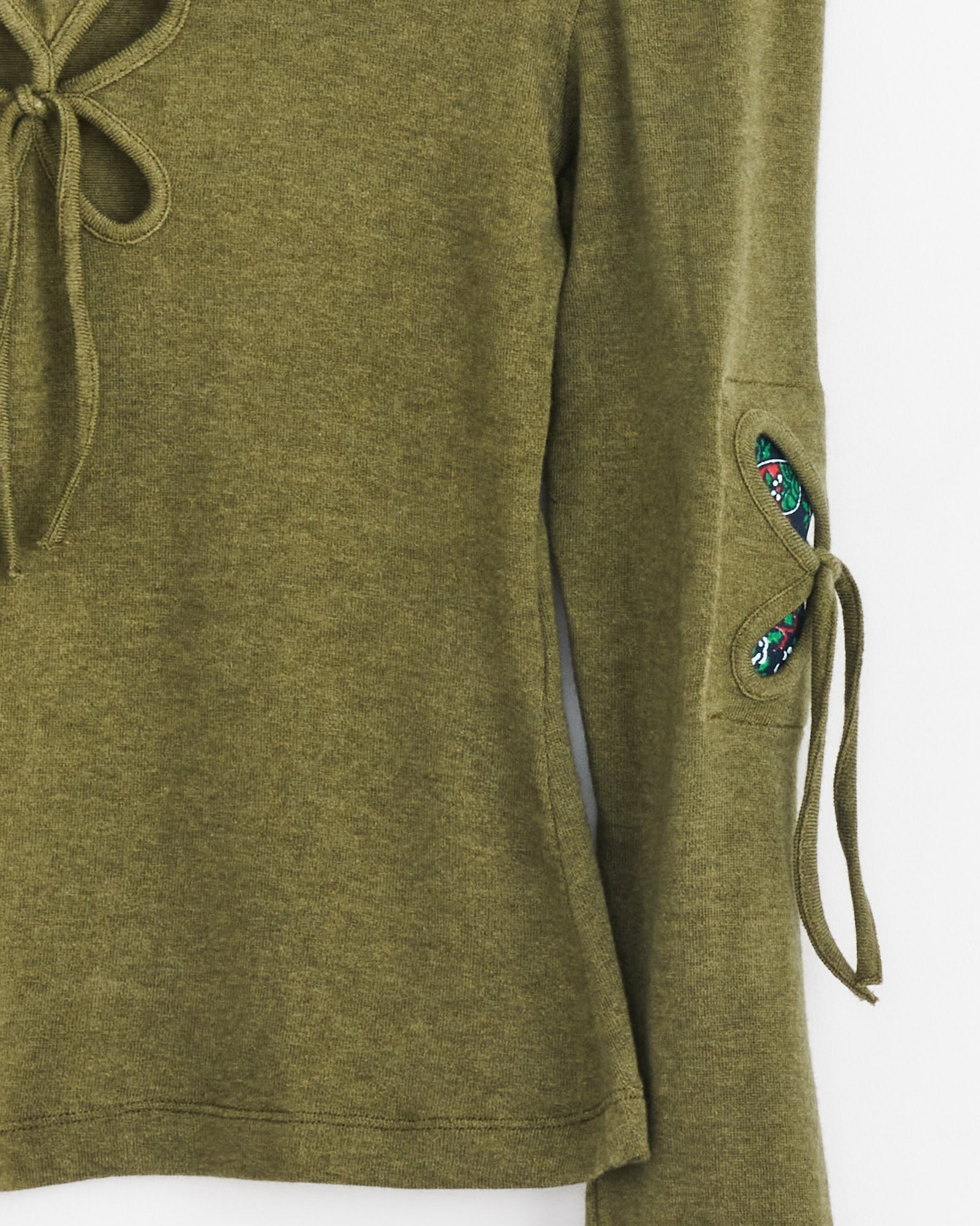 Petal Patches Top in Swamp Green by J. Kim features long sleeves, a lace-up neckline and sleeve detail, plus a small embroidered floral accent at the sleeve opening. The fabric is soft with a subtle texture.