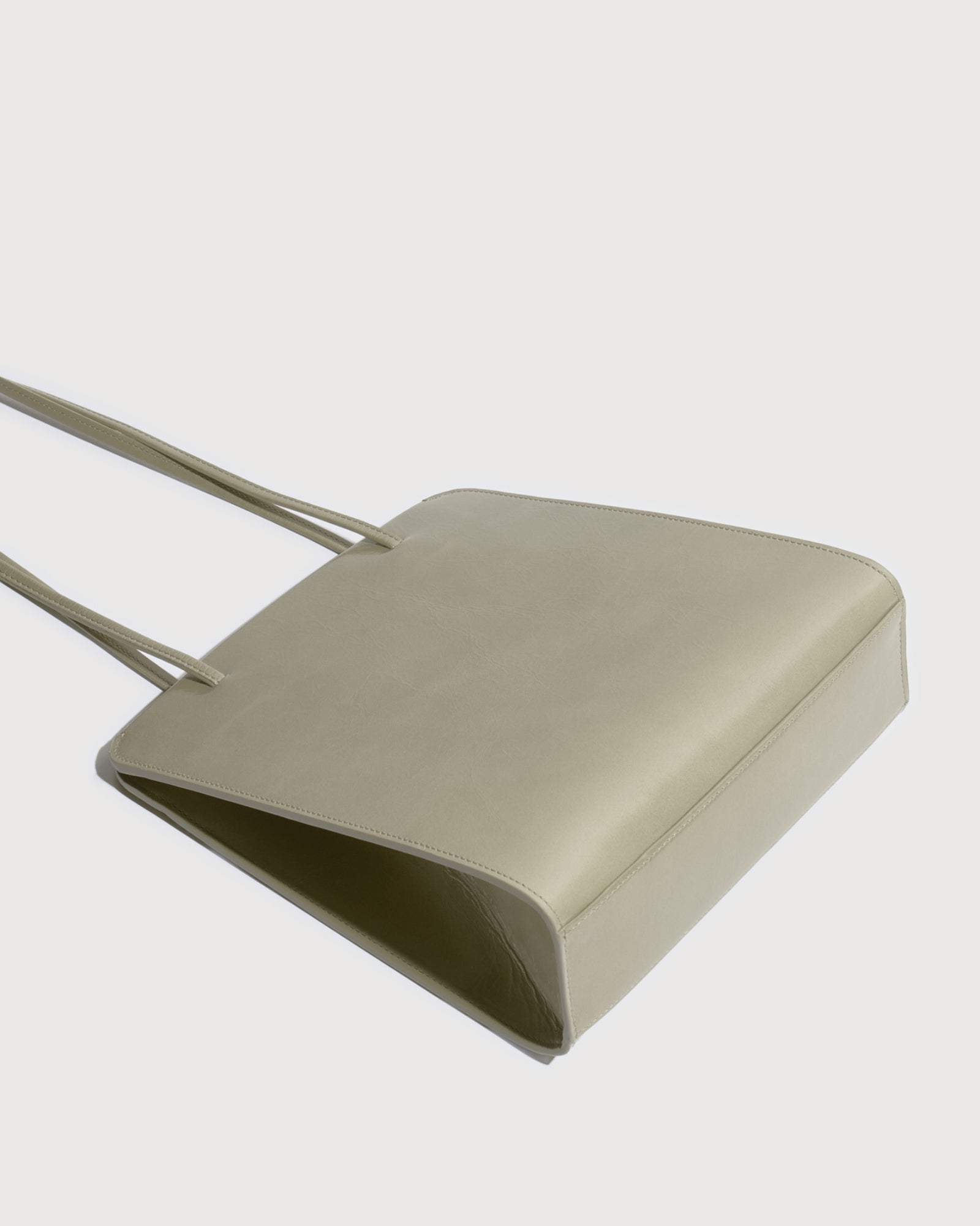 The FANE Lisse Bag in Oyster Glossy Wrinkled features a minimalist, slim rectangular shape with two thin straps, crafted from glossy leather and shown on a white background.