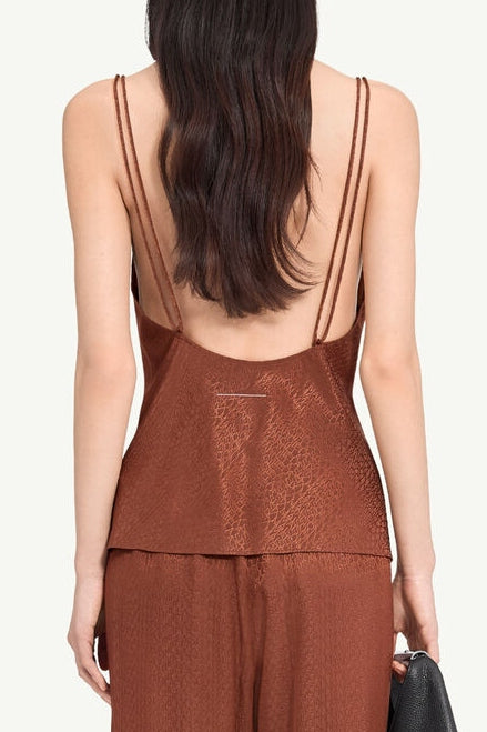 A woman wears the MM6 Maison Margiela Jacquard Top in Light Brown with double thin straps and an open back, paired with matching loose pants, holding a black textured clutch.