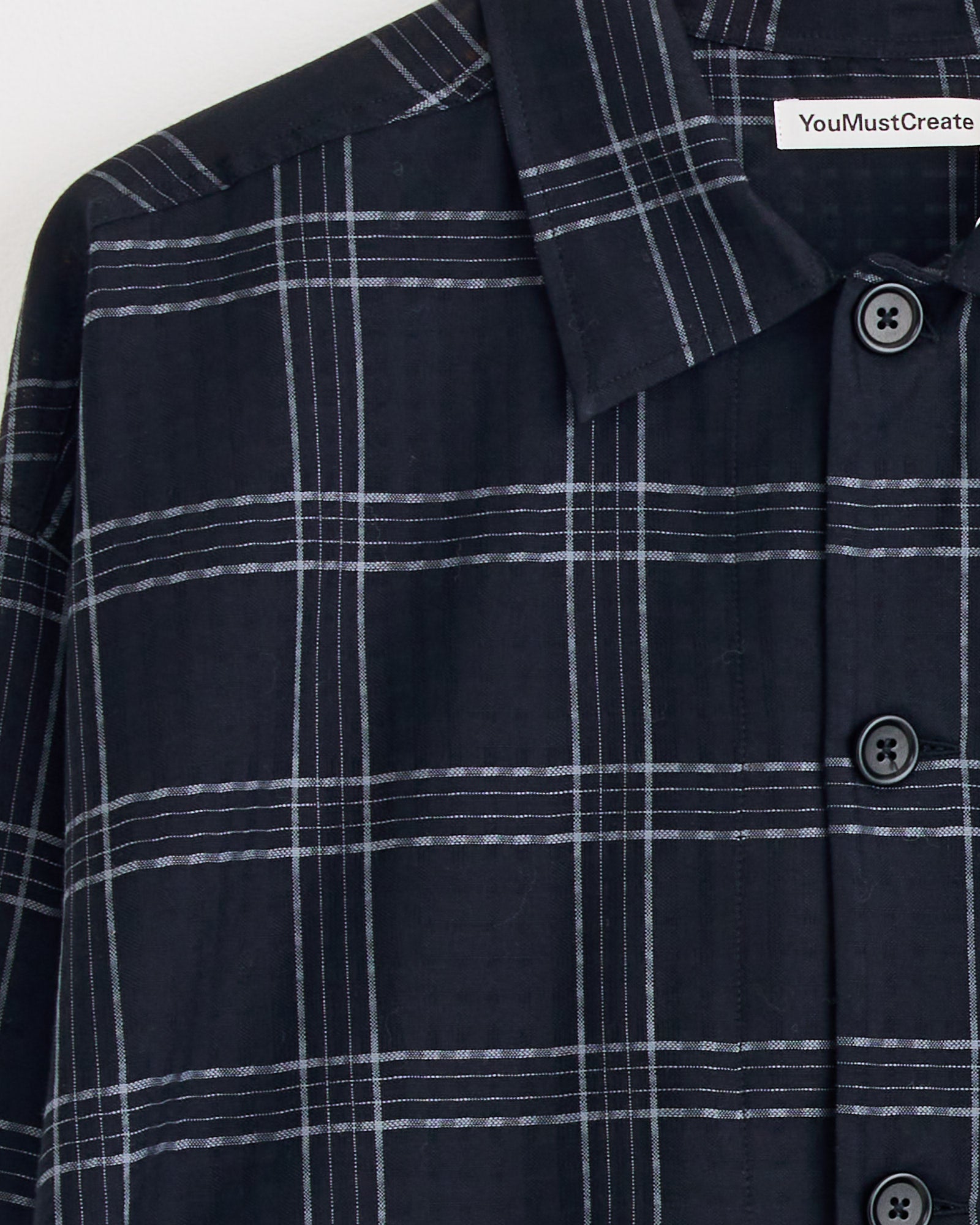 Close-up of the YMC PJ Overshirt in Black/Grey, featuring a plaid pattern and black buttons. For fit or sizing questions, check the garment tag or use our online chat for help.