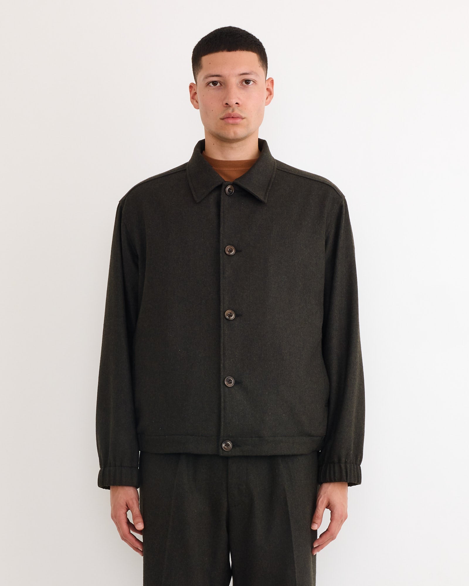 A person stands against a plain white background wearing the SMOCK Blakey Jacket in Cashmere Wool Dark Olive with matching pants. Their arms are relaxed at their sides, and they are looking straight ahead.