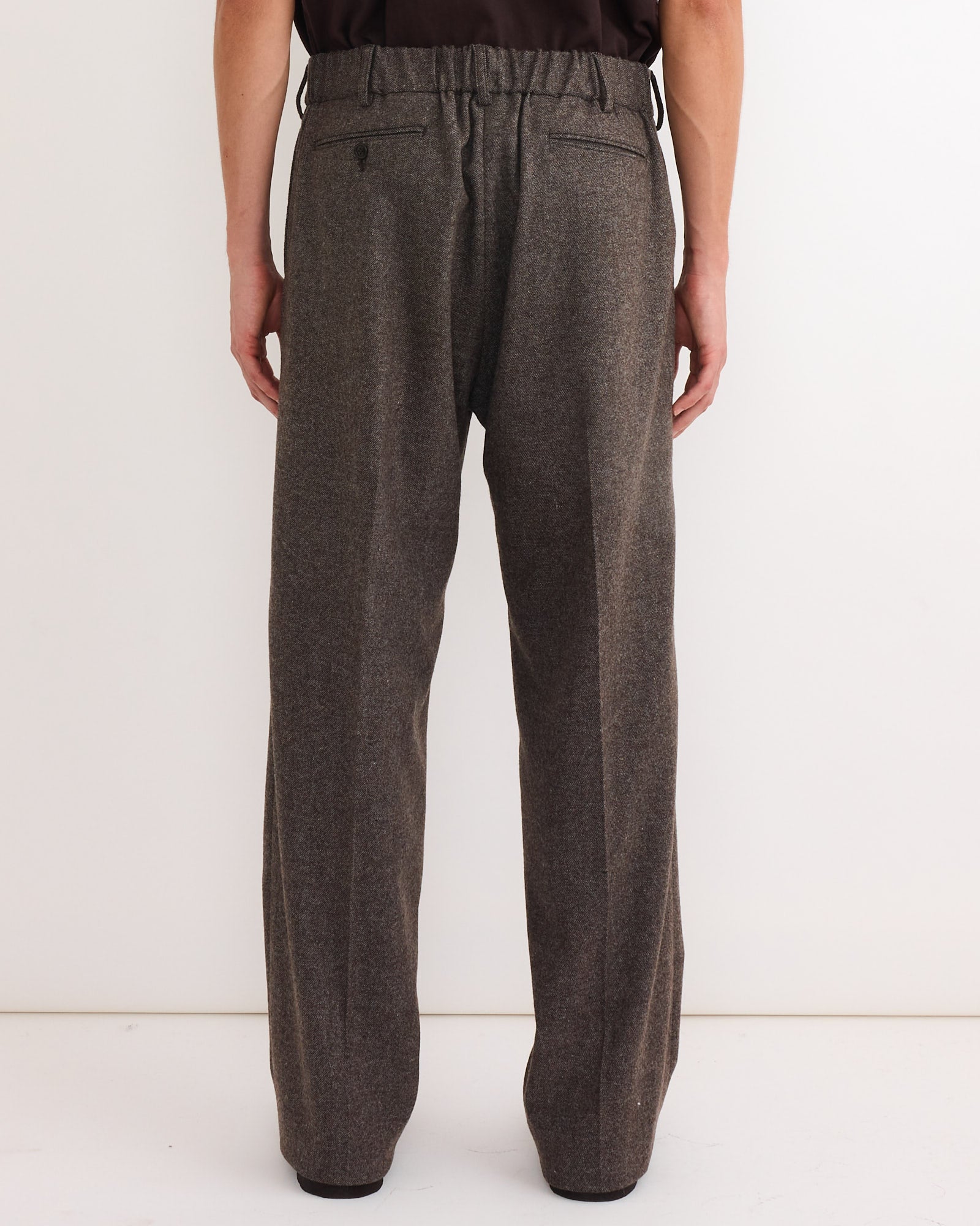 A person faces away from the camera wearing SMOCK’s loose West Coast Pant in Cashmere Wool Brown and a dark shirt, set against a plain white background.