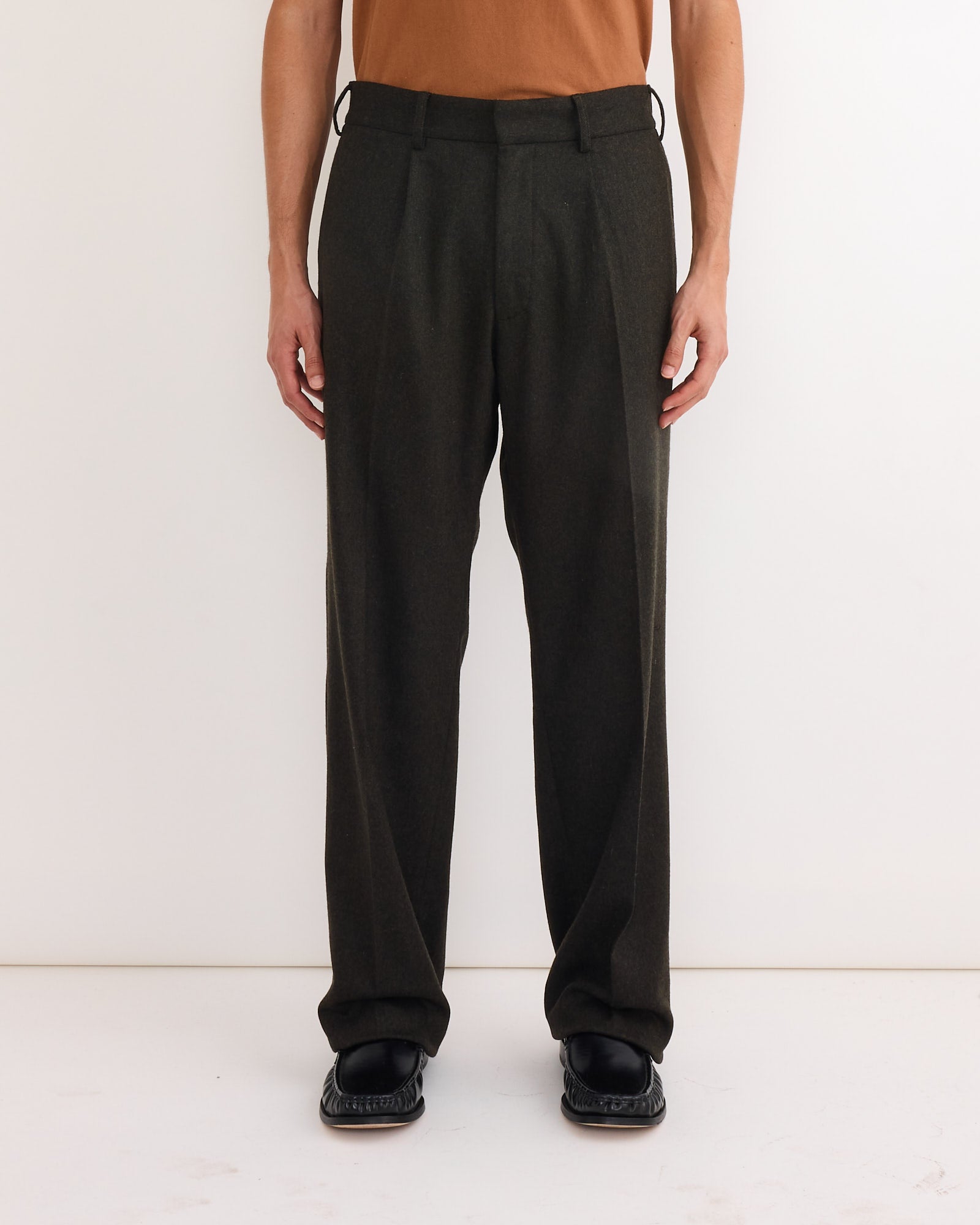 A person models the SMOCK West Coast Pant in Cashmere Wool Dark Olive with black shoes against a plain white background; their brown shirt and the image are cropped at the shoulders.
