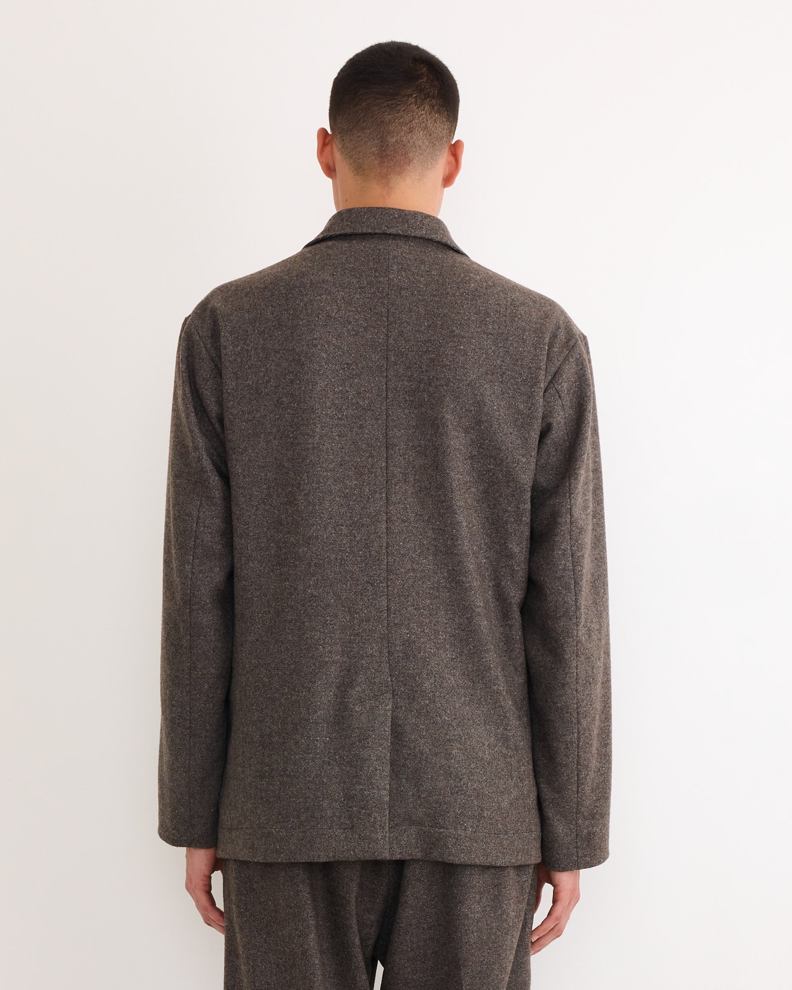 A person with short dark hair, facing away from the camera, wears the SMOCK Blazer in Cashmere Wool Brown and matching trousers, made in Los Angeles, against a plain white background.